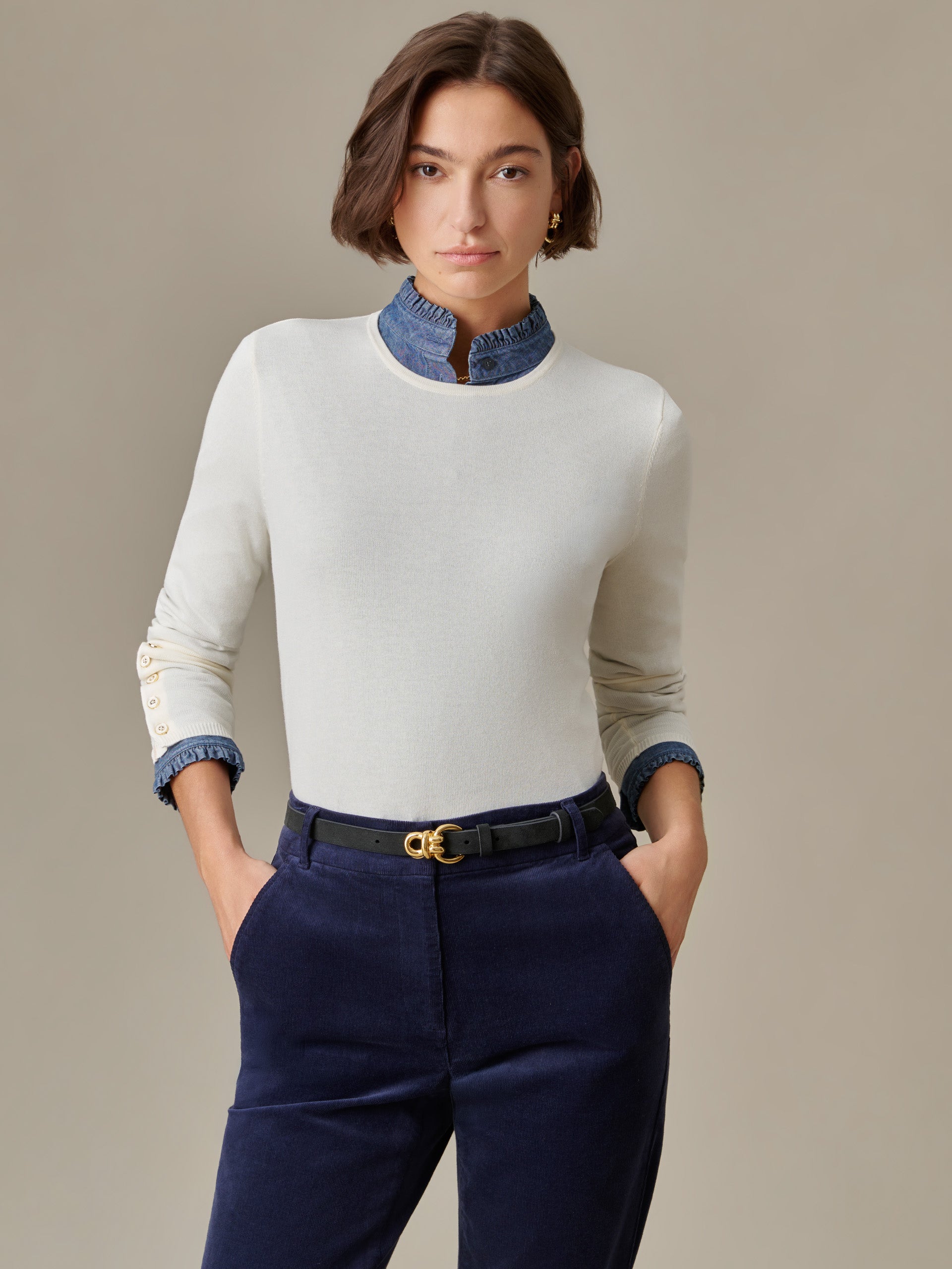 Woman wearing a J.McLaughlin Jamey Sweater in white with gold buttons on sleeves, paired with navy pants and a black belt, showcasing timeless style and craftsmanship.