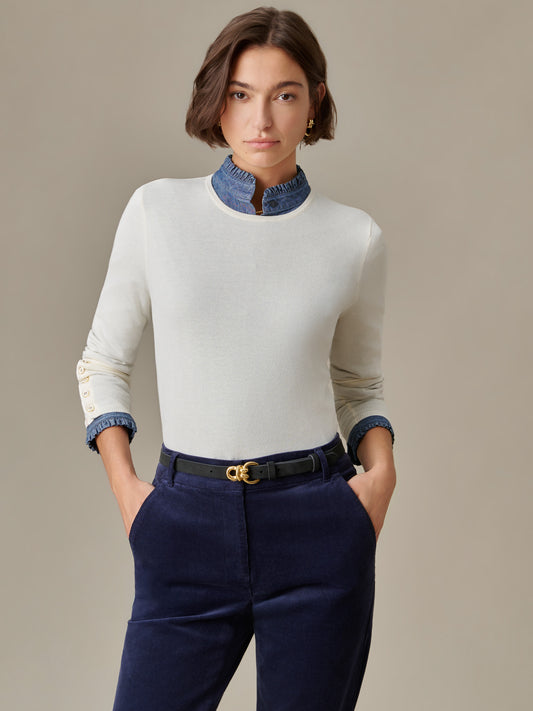 Woman wearing a J.McLaughlin Jamey Sweater in white with gold buttons on sleeves, paired with navy pants and a black belt, showcasing timeless style and craftsmanship.