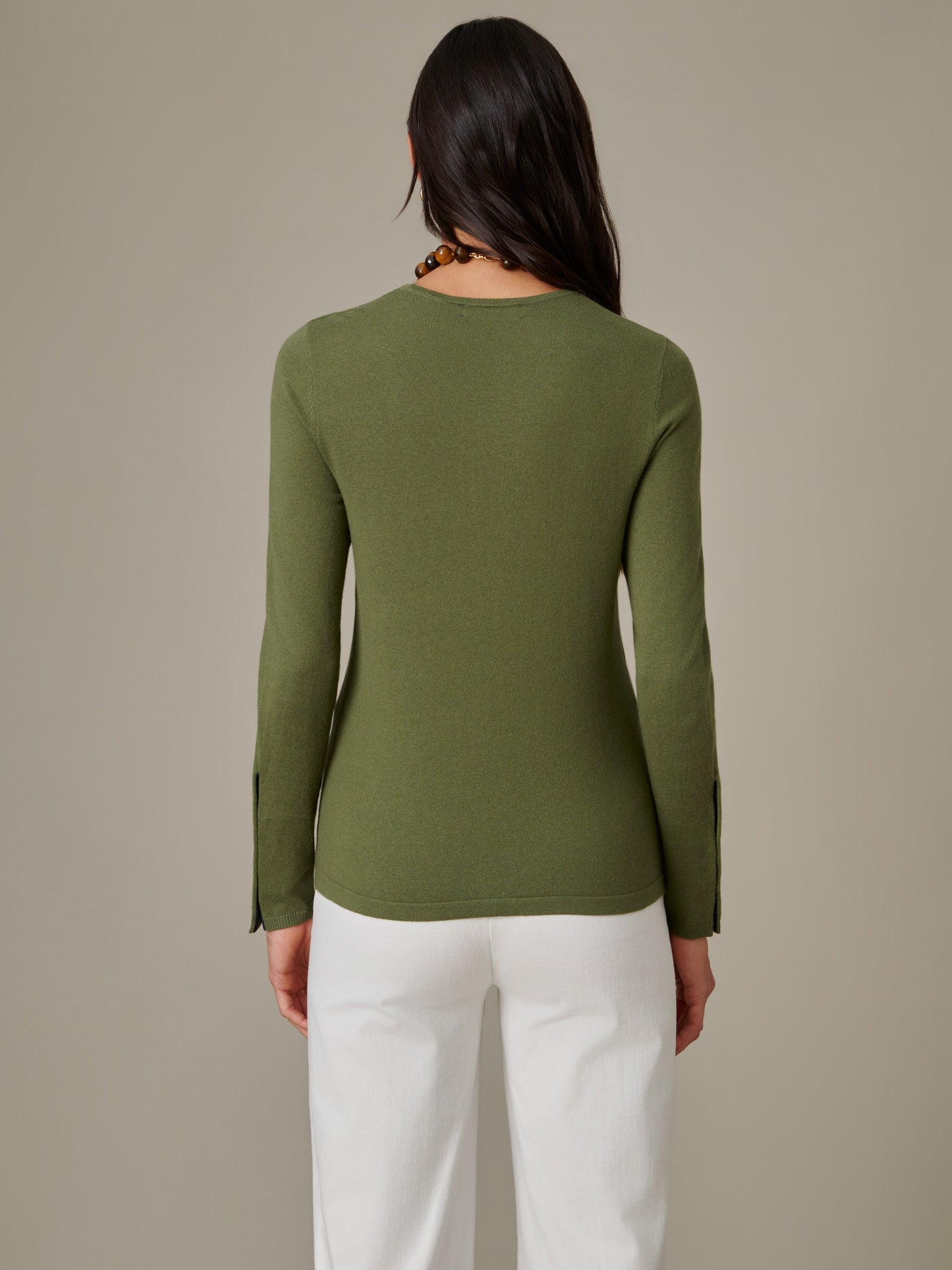 Back view of a woman wearing an olive green Jamey Sweater by J.McLaughlin, showcasing the sweater’s sleek fit and timeless design paired with white pants.