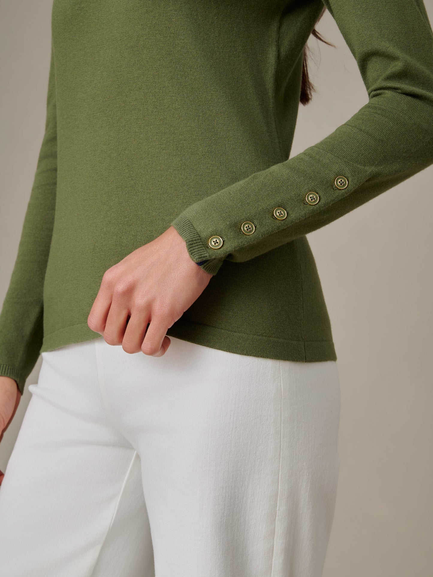 Close-up of a person wearing a Jamey Sweater in olive green by J.McLaughlin, featuring button details on the sleeve, styled with white pants for a timeless, effortlessly stylish look.
