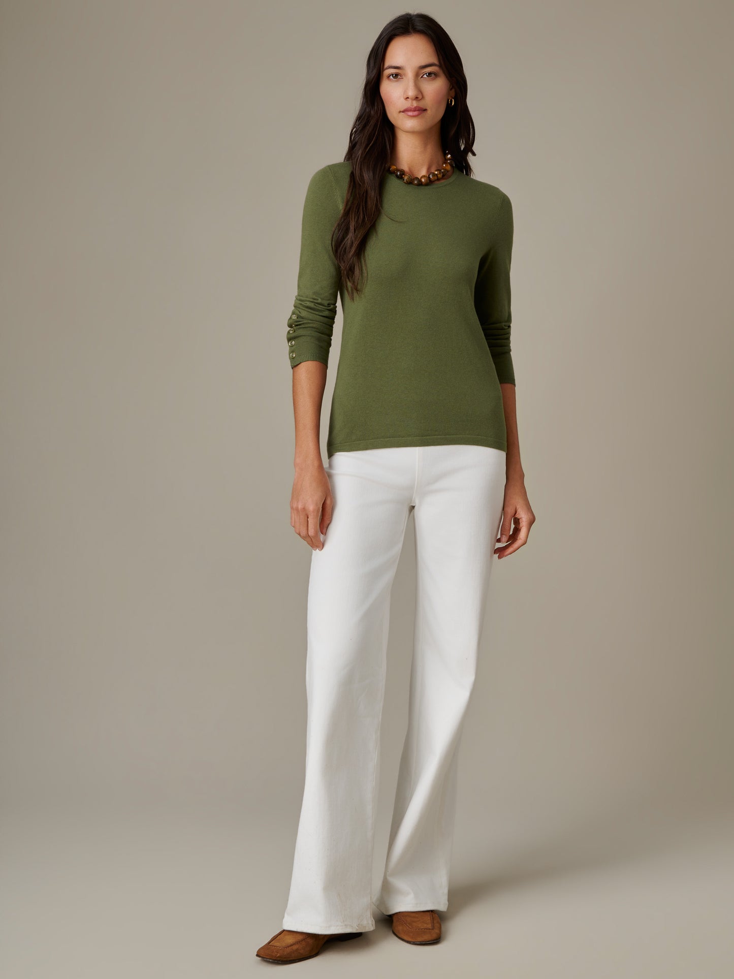Woman wearing an olive green Jamey Sweater by J.McLaughlin paired with white wide-leg pants and brown shoes, showcasing effortless style and timeless design.