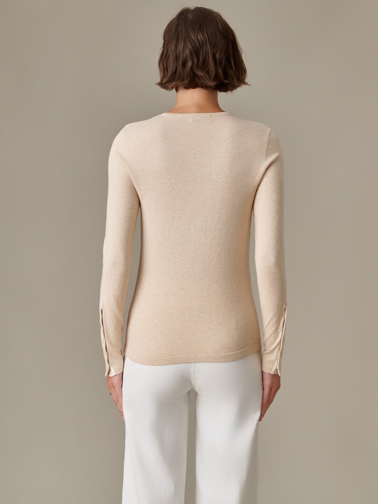 Back view of a woman wearing a beige Jamey Sweater by J.McLaughlin paired with white pants, showcasing the sweater's sleek, timeless design and button details on the sleeves.