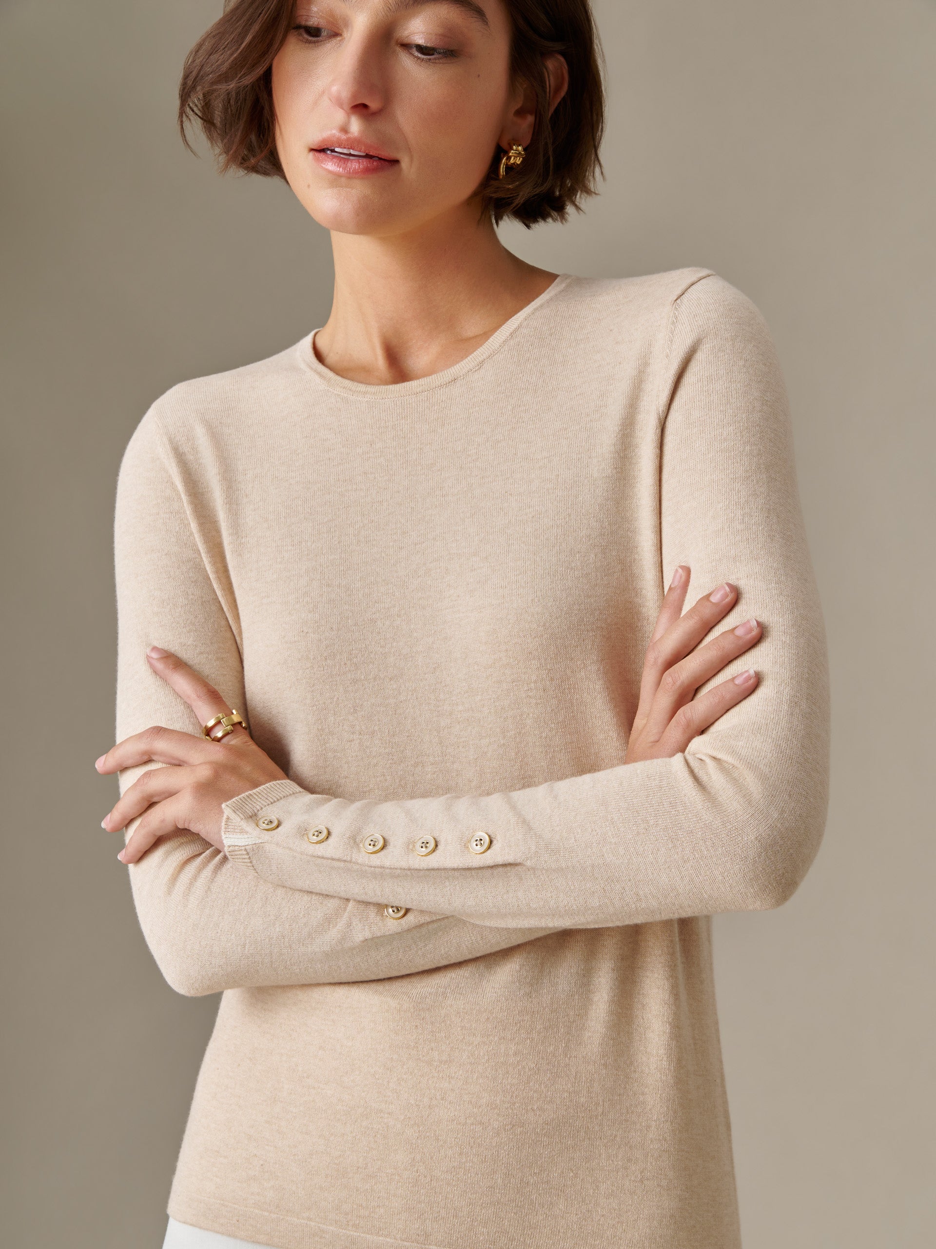 Woman wearing a beige long-sleeve Jamey Sweater by J.McLaughlin, featuring button details on the cuff, showcasing an effortlessly stylish and timeless design.
