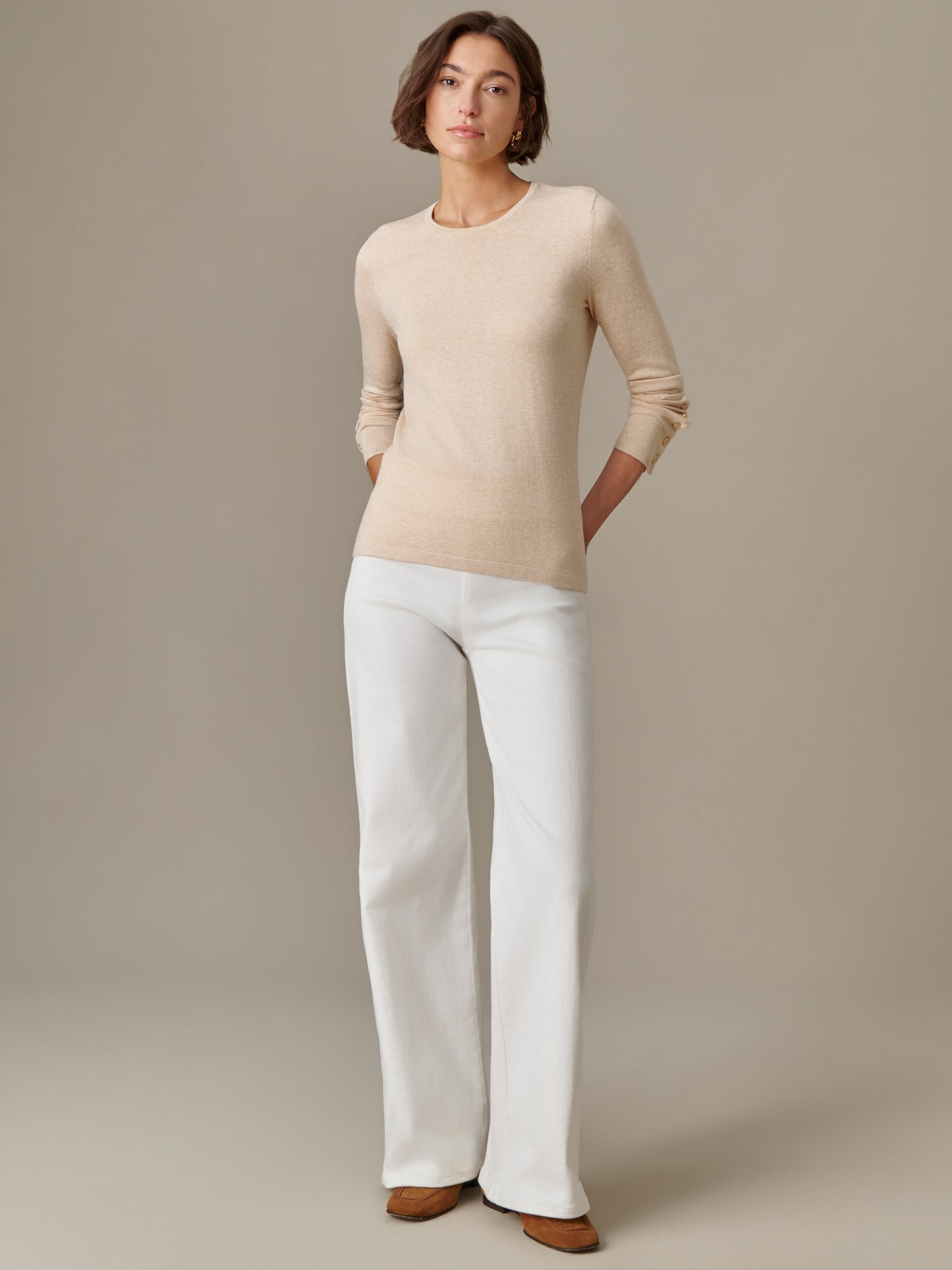 A woman wearing the Jamey Sweater by J.McLaughlin in a soft beige tone paired with white wide-leg pants, showcasing effortlessly stylish and enduring designs.