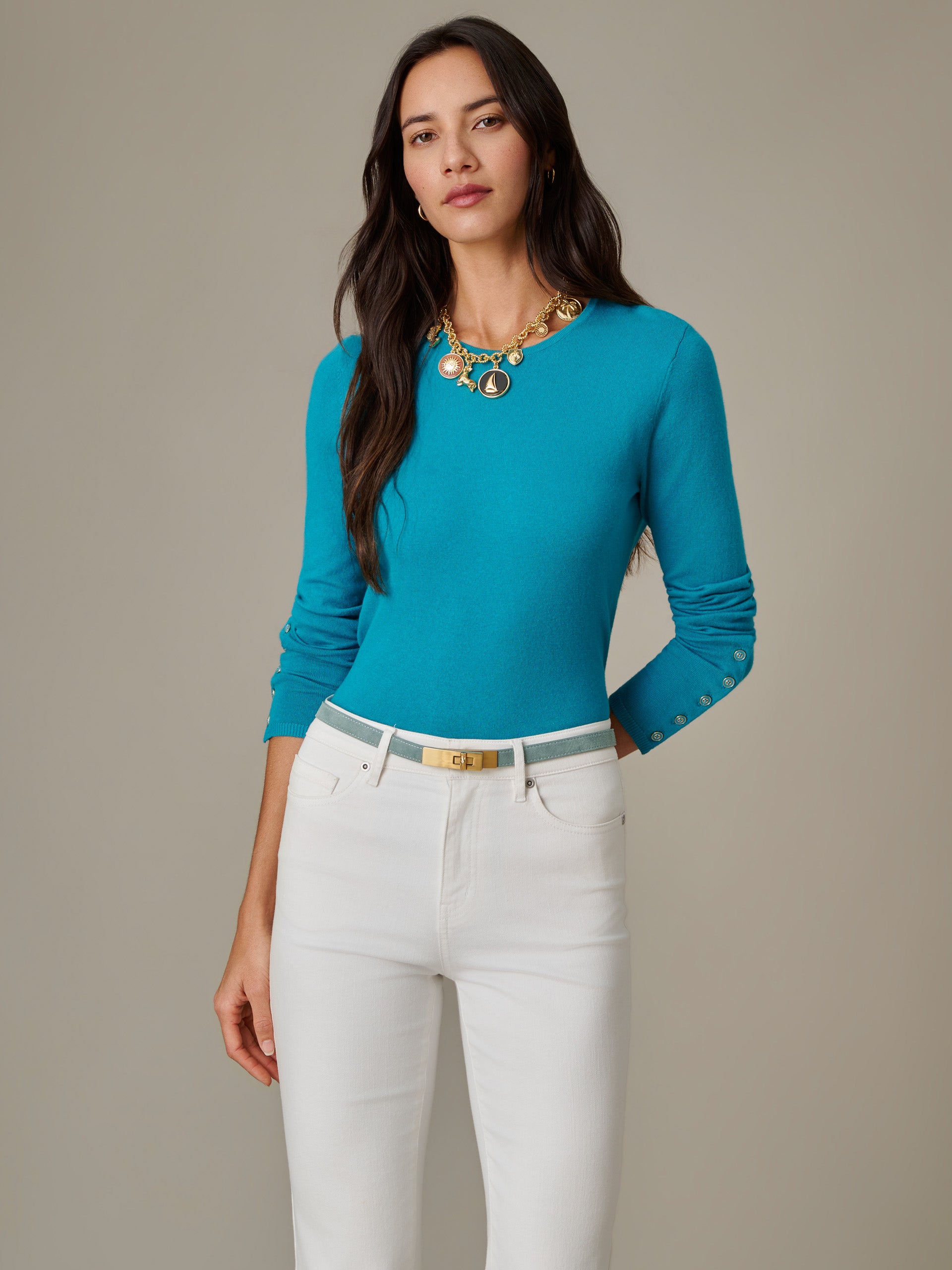 Woman wearing a vibrant blue Jamey Sweater by J.McLaughlin paired with white pants and a gold-accented belt, showcasing a timeless and effortlessly stylish look.