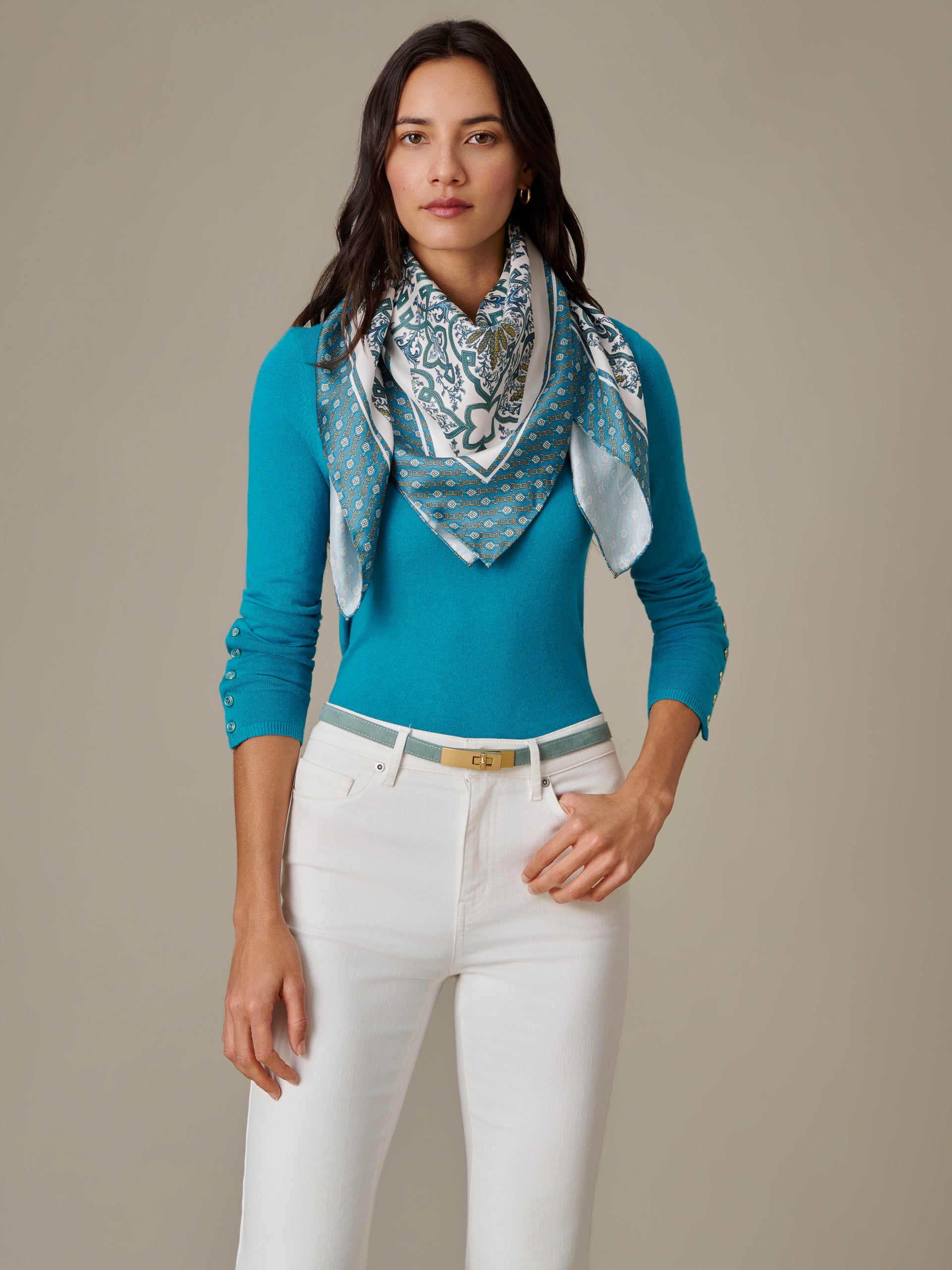 Woman wearing a vibrant blue Jamey Sweater by J.McLaughlin paired with a patterned scarf and white pants, showcasing effortlessly stylish and enduring designs.
