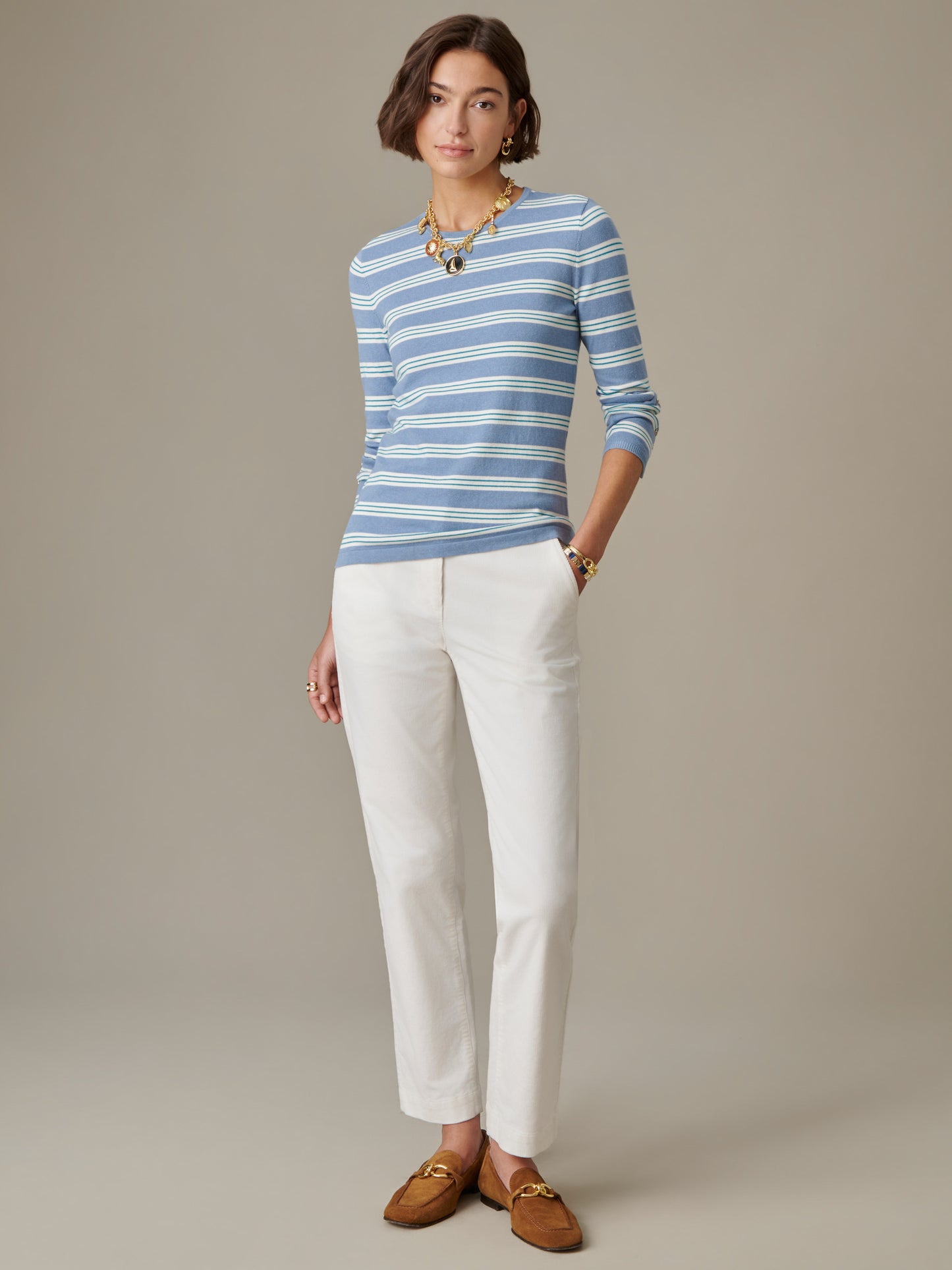 Woman wearing a J.McLaughlin Jamey Sweater in Stripe paired with white pants and brown loafers, showcasing timeless style with classic, enduring design.