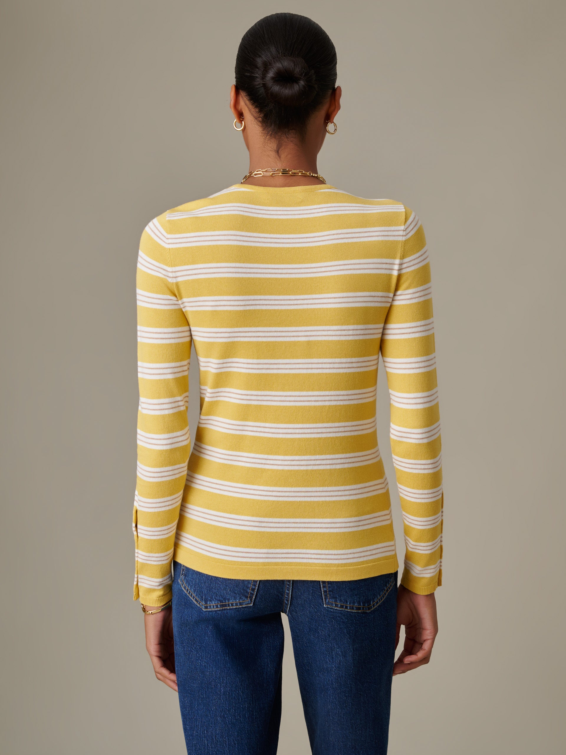 Woman seen from behind wearing a J.McLaughlin Jamey Sweater in Stripe in yellow and white, paired with classic blue jeans, showcasing timeless style and quality craftsmanship.