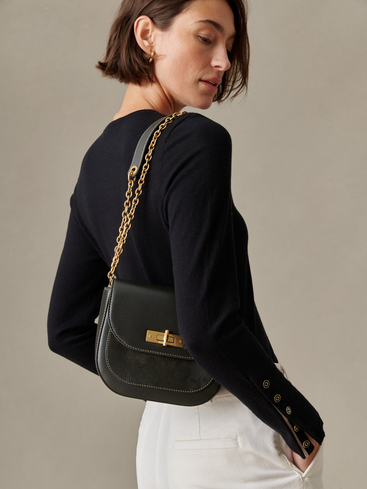 Woman wearing a black long-sleeve top and white pants carrying The Waverly Leather Handbag by J.McLaughlin with a gold chain strap, showcasing an effortlessly stylish and timeless design.