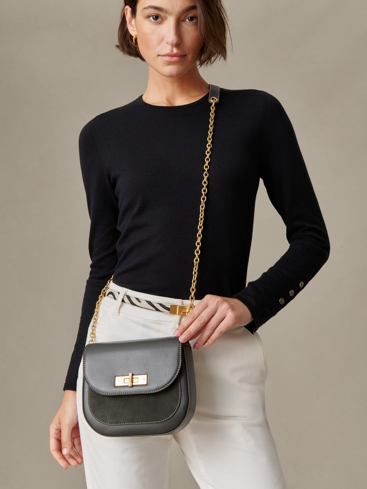 Woman wearing a black long-sleeve top and white pants holding The Waverly Leather Handbag by J.McLaughlin with gold chain strap, showcasing an effortlessly stylish, timeless design.
