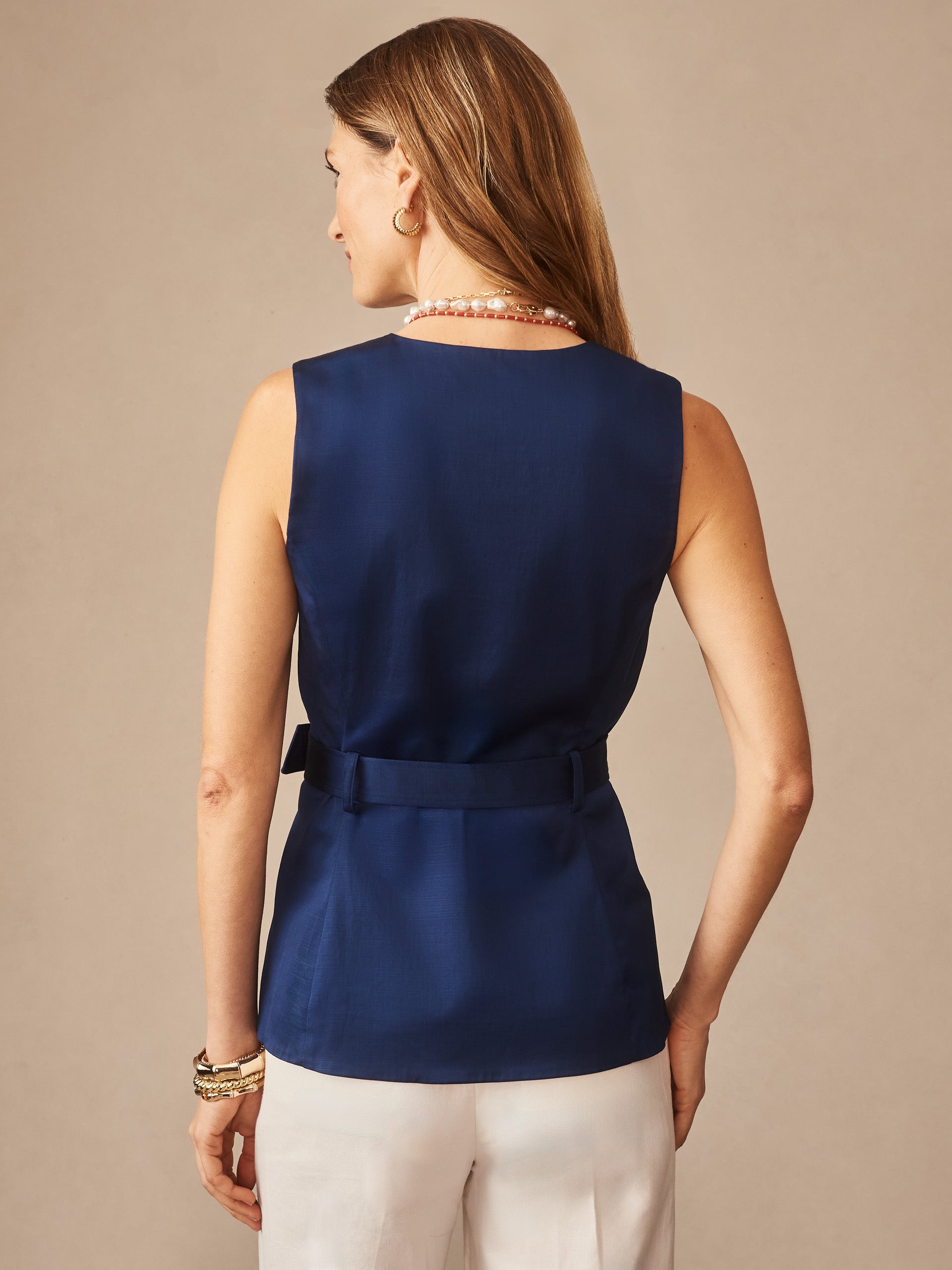 A woman seen from the back wearing a navy Jennifer Dupioni Cotton Vest by J.McLaughlin, paired with white pants and layered bracelets, showcasing effortlessly stylish, enduring designs and innovative fabrics.