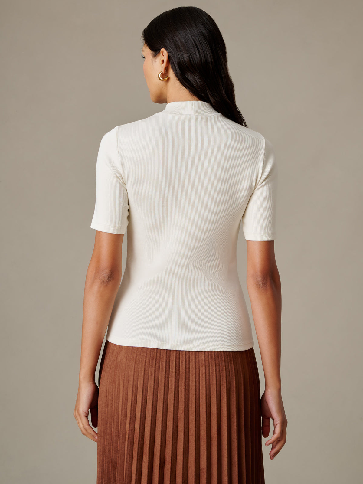 J.McLaughlin Jess Ribbed Top in ivory shown from the back with a mock neckline short sleeves and fitted ribbed texture paired with a pleated brown skirt