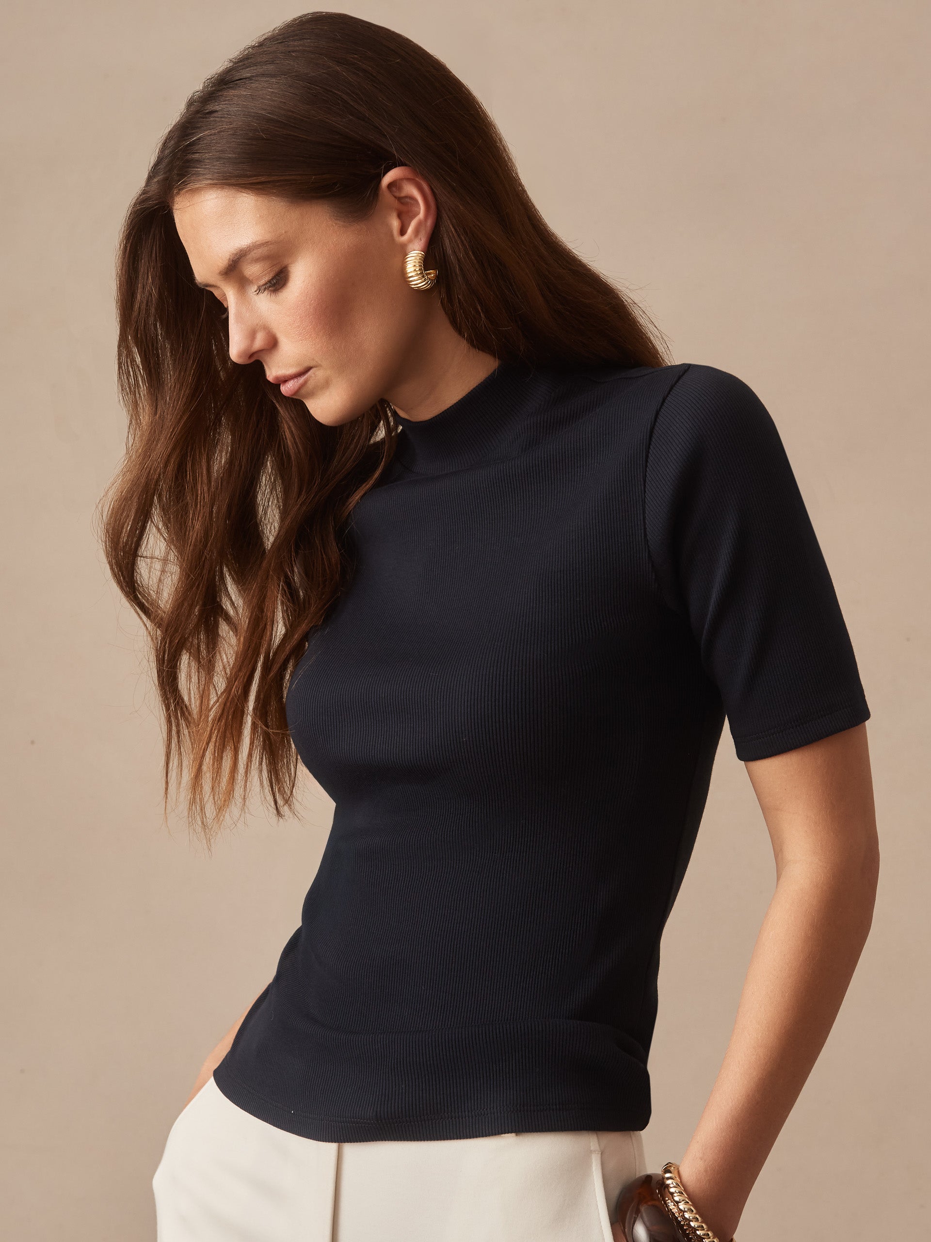 Woman wearing a navy Jess Ribbed Top by J.McLaughlin, featuring a sleek high neckline and short sleeves, embodying effortlessly stylish, enduring designs and innovative fabrics.