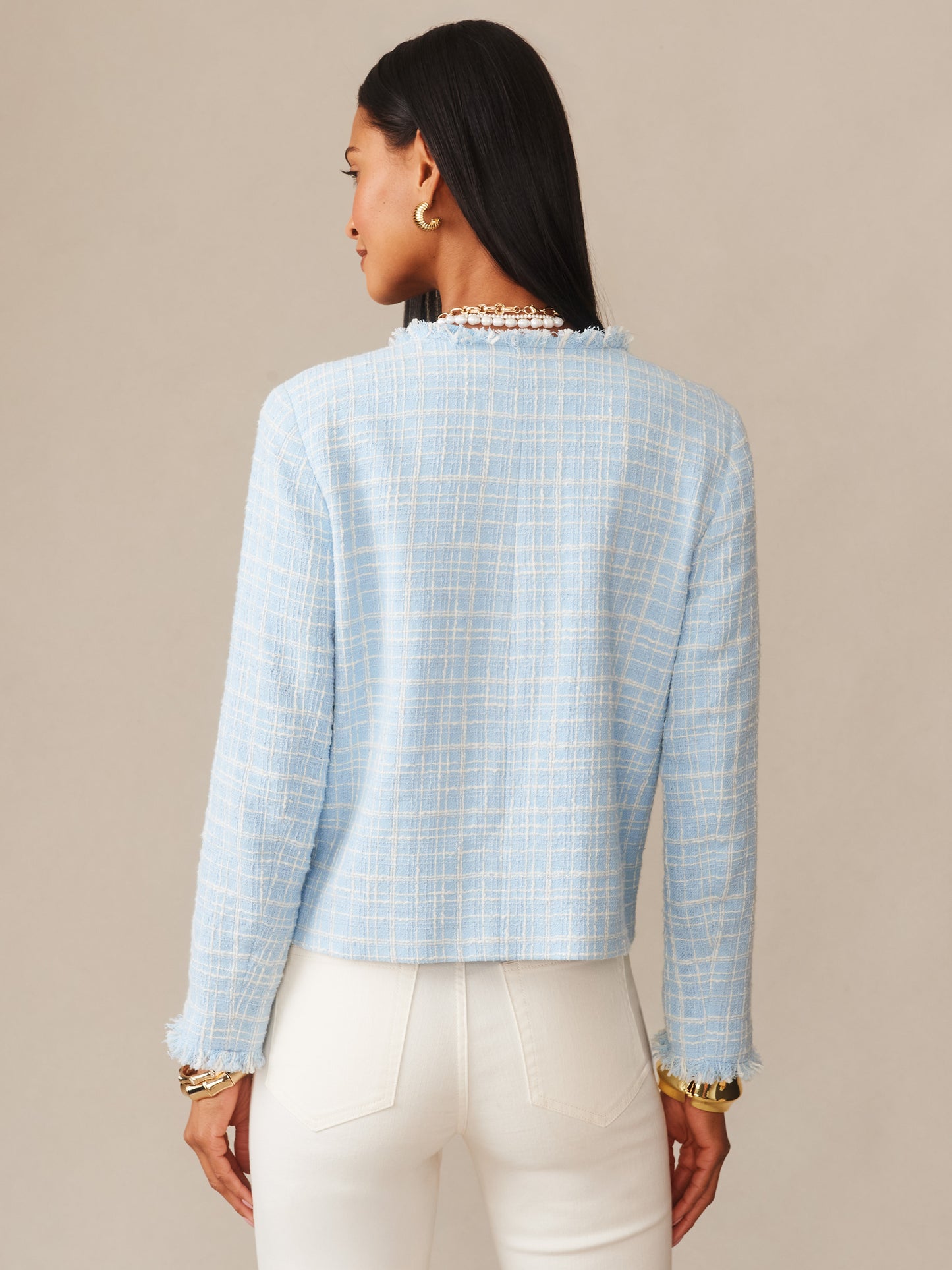 Woman wearing an Abigail Bouclé Jacket in Mini Window Pane by J.McLaughlin in soft blue, styled with gold jewelry and white pants, showcasing effortlessly stylish, enduring designs.