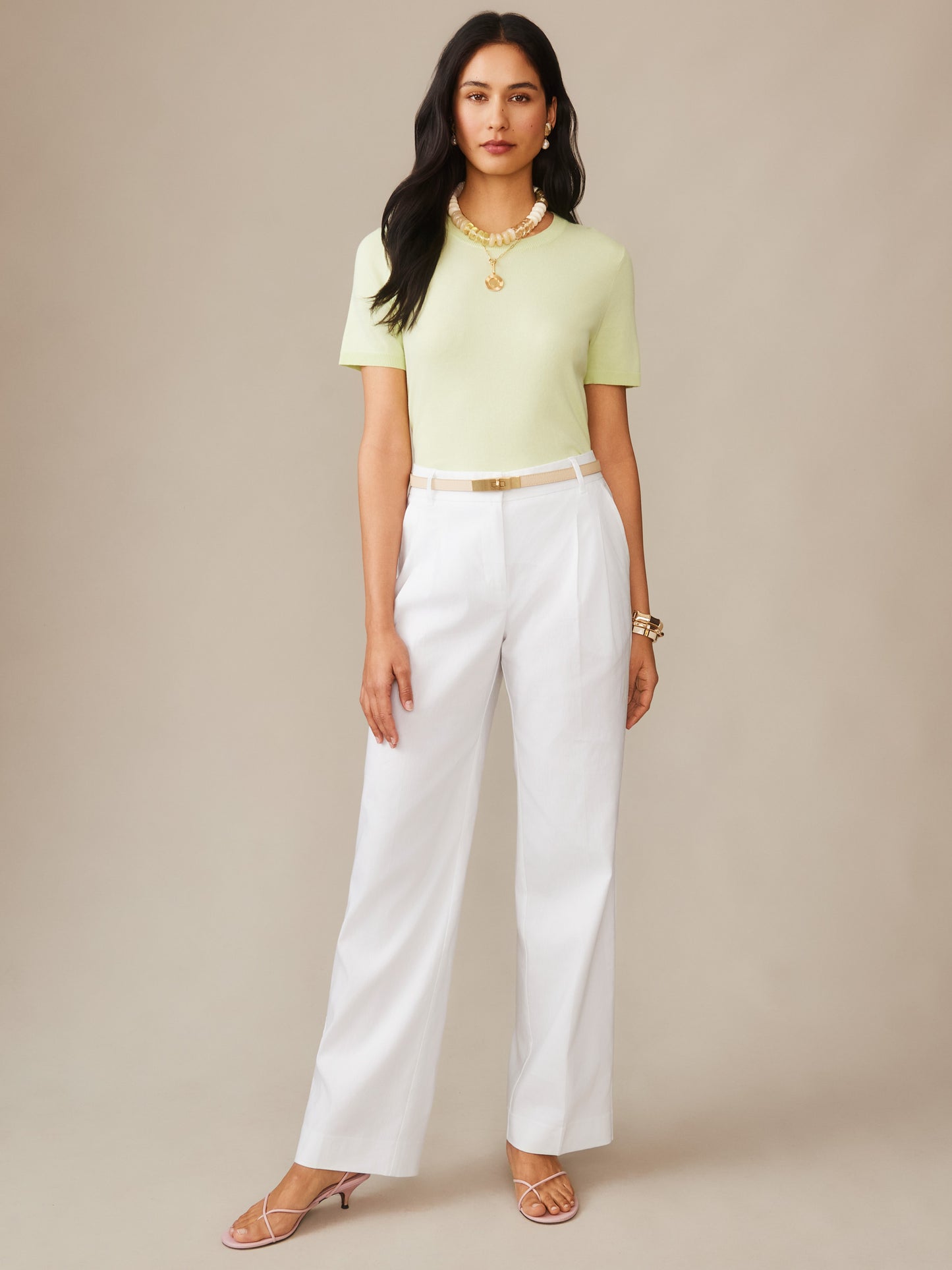 Woman wearing a light green Joelle Sweater by J.McLaughlin paired with white tailored pants and strappy sandals, embodying effortlessly stylish, enduring designs and a legacy of timeless fashion.