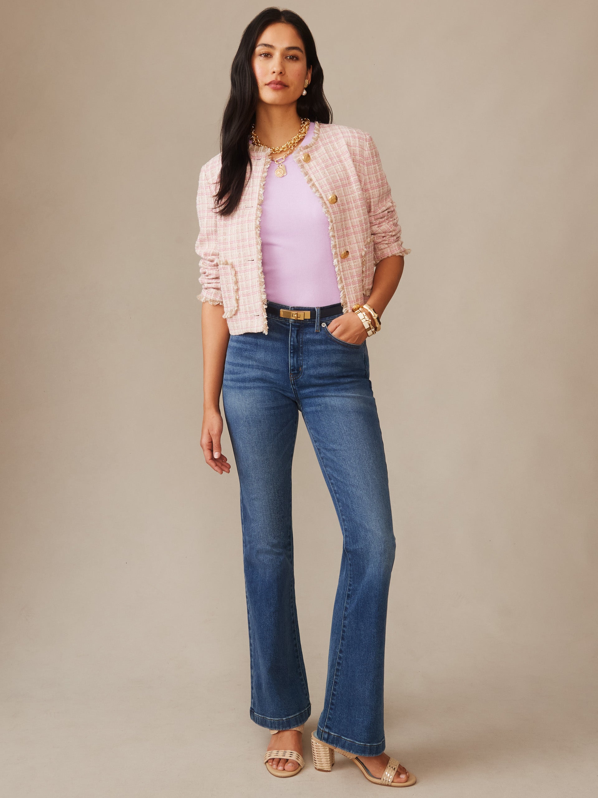 Woman wearing a pink Abigail Bouclé Jacket in Mini Window Pane by J.McLaughlin over a lavender top paired with high-waisted blue jeans and sandals, showcasing effortlessly stylish, enduring designs.