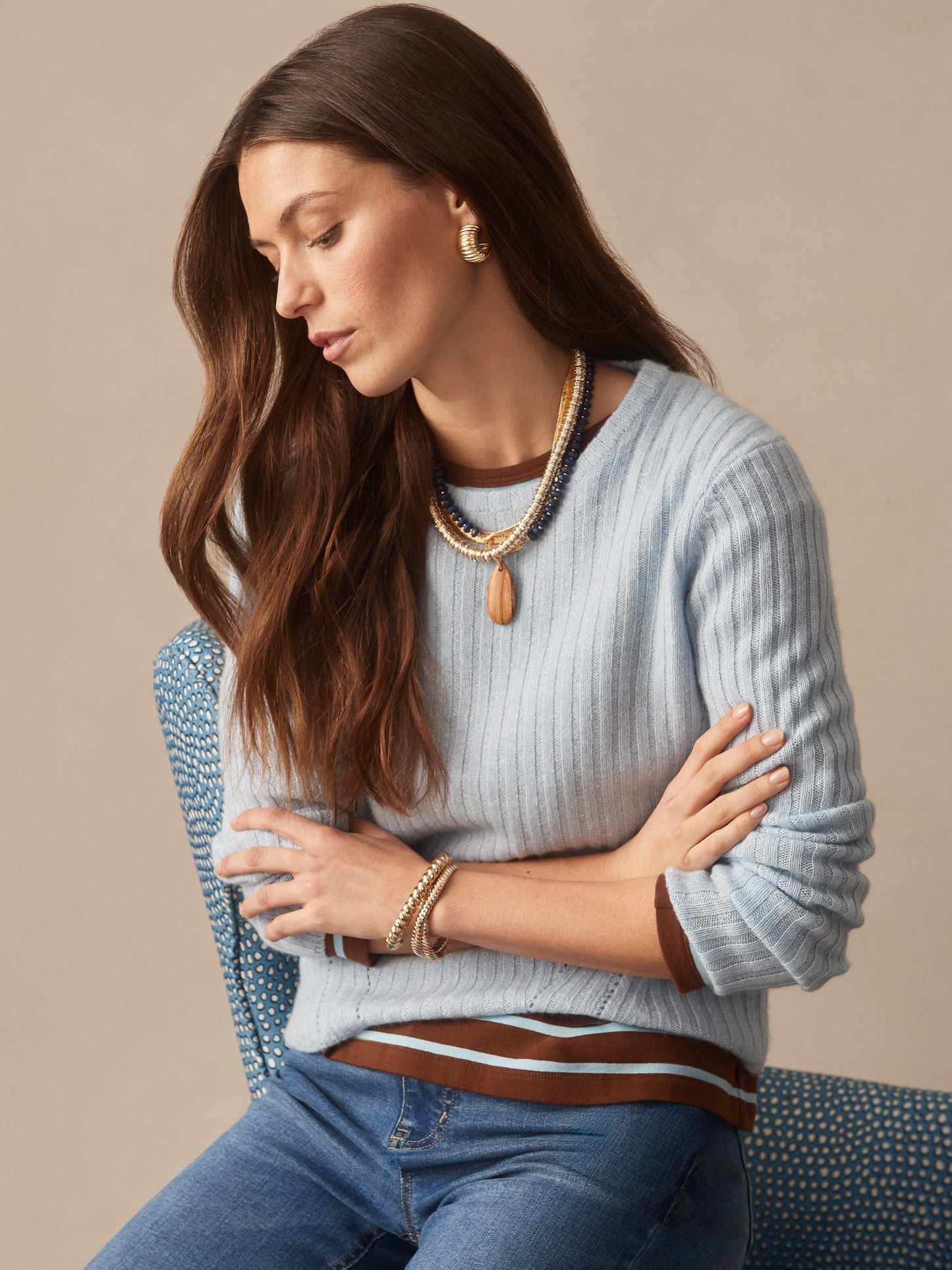 Woman wearing a soft blue Josephine Sweater by J.McLaughlin paired with layered necklaces and bracelets, showcasing effortlessly stylish, enduring designs with innovative fabrics.