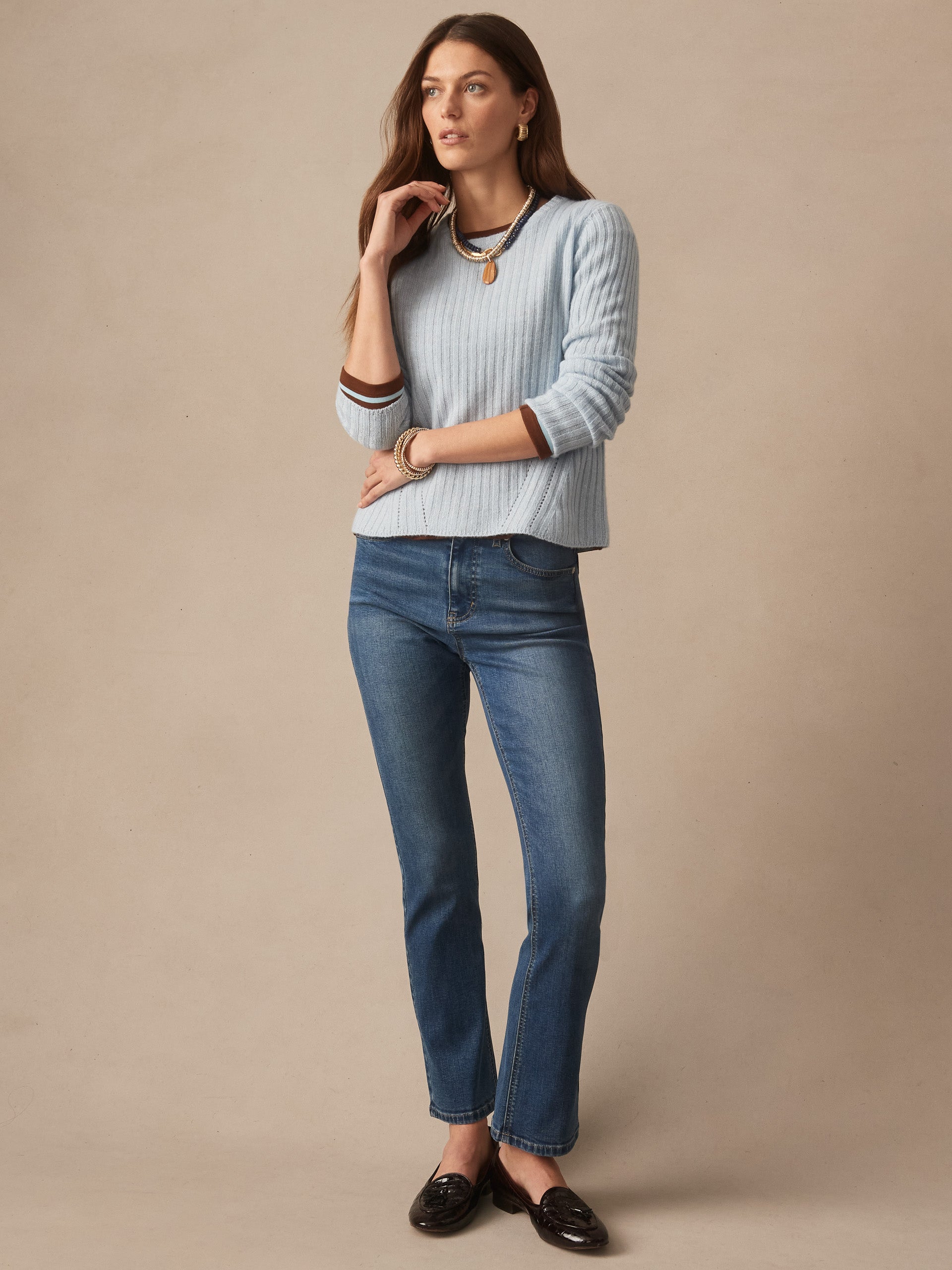 Woman wearing a soft blue Josephine Sweater by J.McLaughlin, paired with classic blue jeans and loafers, showcasing effortlessly stylish, enduring designs and innovative fabrics.