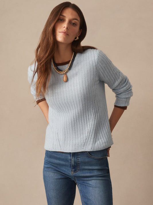 Woman wearing a soft blue Josephine Sweater by J.McLaughlin, styled with layered necklaces and casual jeans, reflecting effortlessly stylish, enduring designs and innovative fabrics.