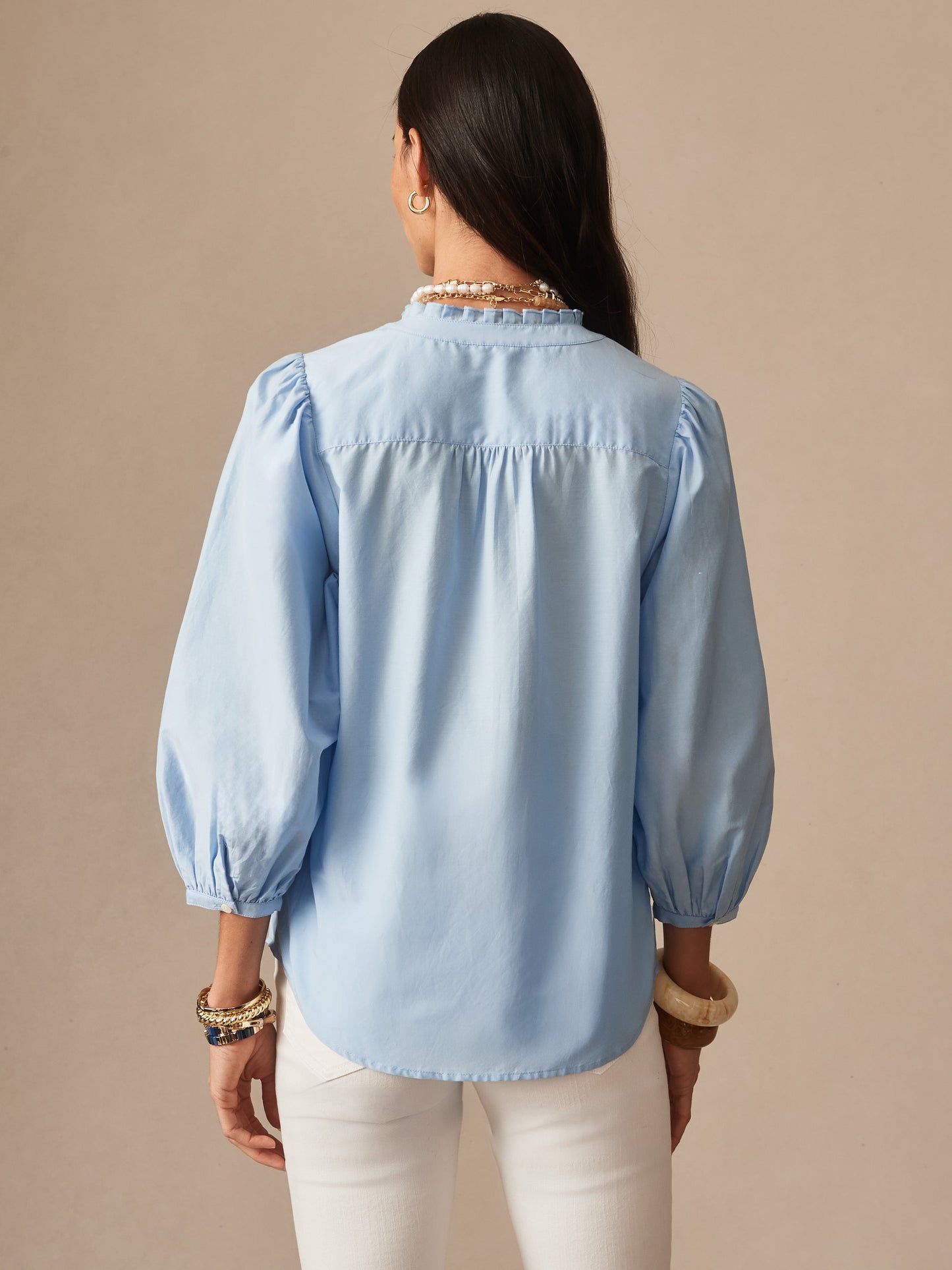 Woman wearing a light blue Josette Blouse by J.McLaughlin, featuring puffed sleeves and a relaxed fit, showcasing effortlessly stylish, enduring designs with a legacy of timeless fashion.