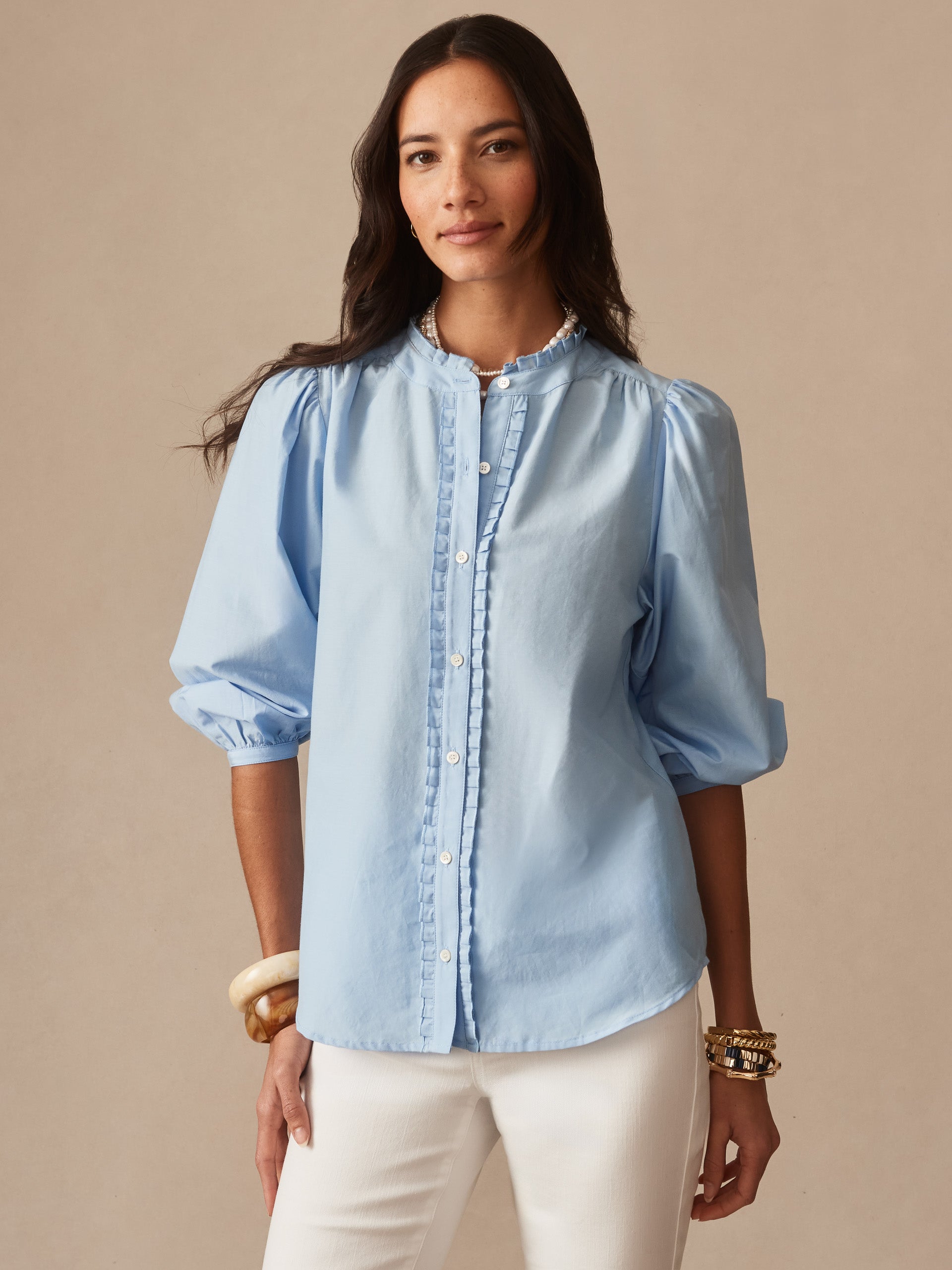 Woman wearing a light blue Josette Blouse by J.McLaughlin featuring puff sleeves and delicate button detailing, showcasing effortlessly stylish, enduring designs in innovative fabrics.