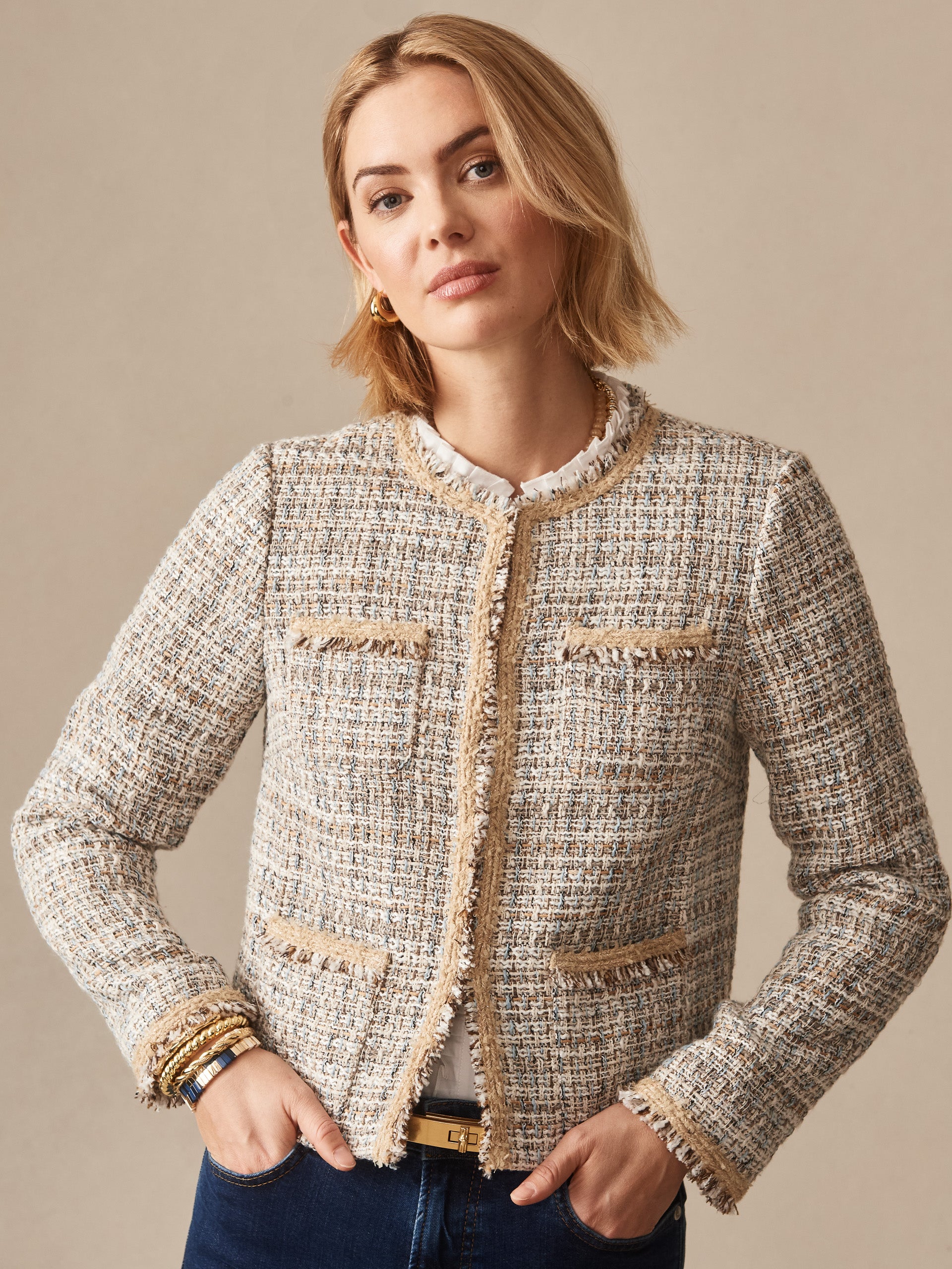 Woman wearing a Martha Tweed Jacket by J.McLaughlin, featuring an effortlessly stylish tweed design with fringe trim, showcasing enduring designs and a legacy of timeless fashion.