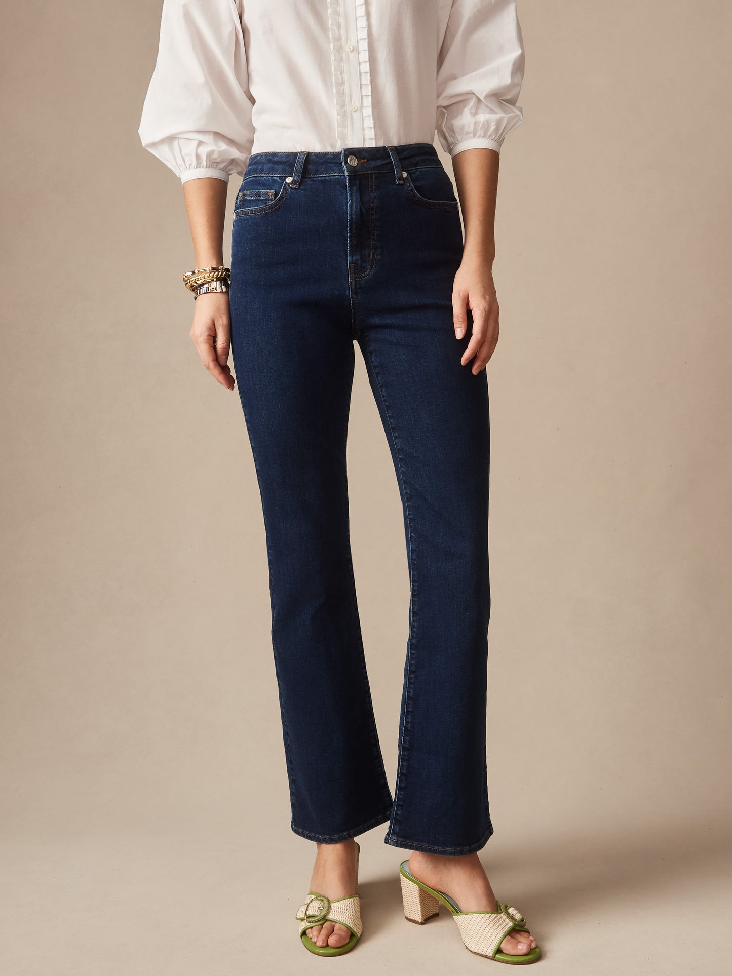 Front view of a person wearing Elvira Jeans by J.McLaughlin in dark wash denim paired with a white puff-sleeve blouse and green heeled sandals, showcasing effortlessly stylish, enduring designs.