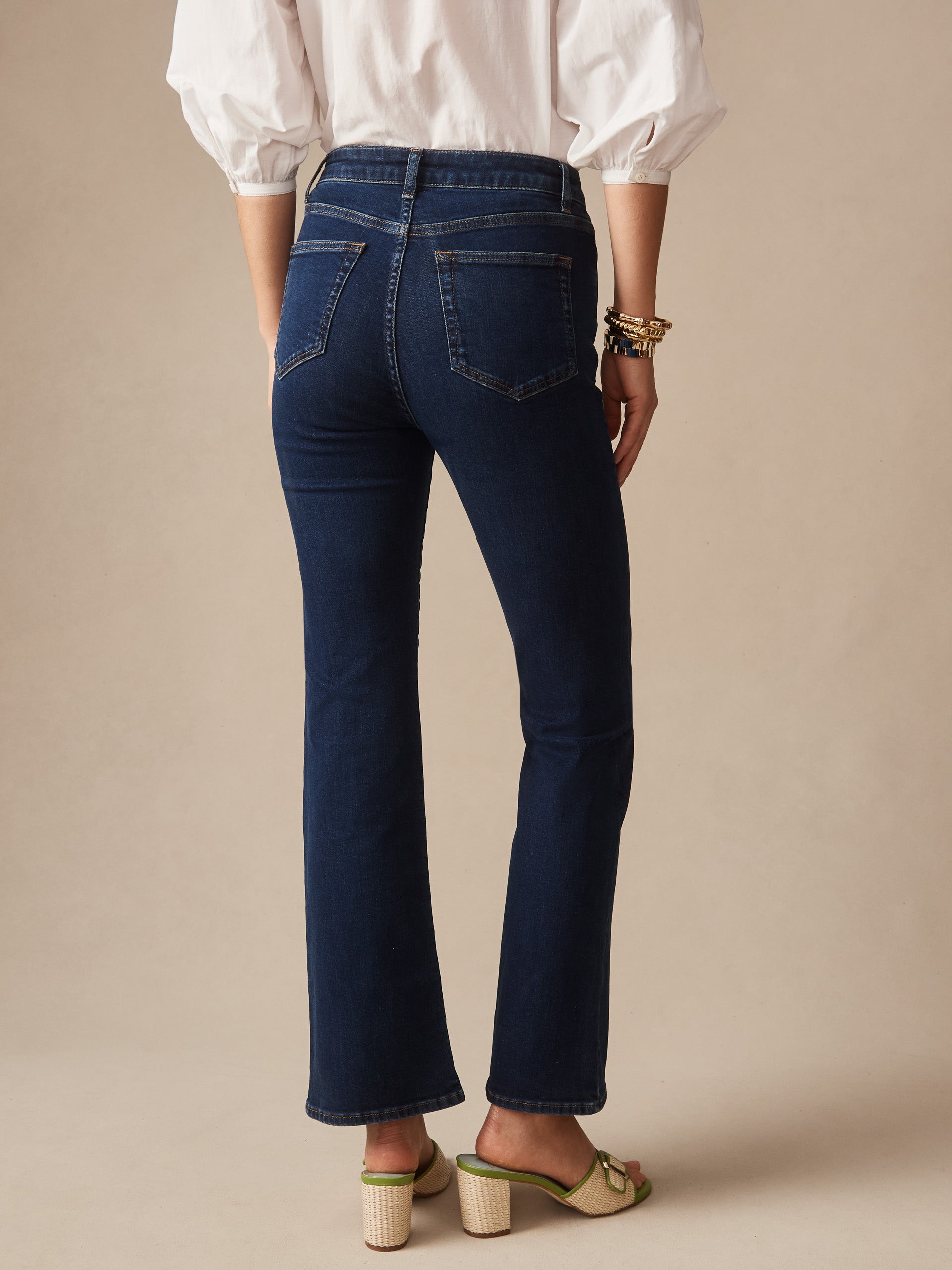 Back view of a person wearing dark blue Elvira Jeans by J.McLaughlin paired with a white blouse and beige heels, showcasing effortlessly stylish, enduring designs and innovative fabrics.