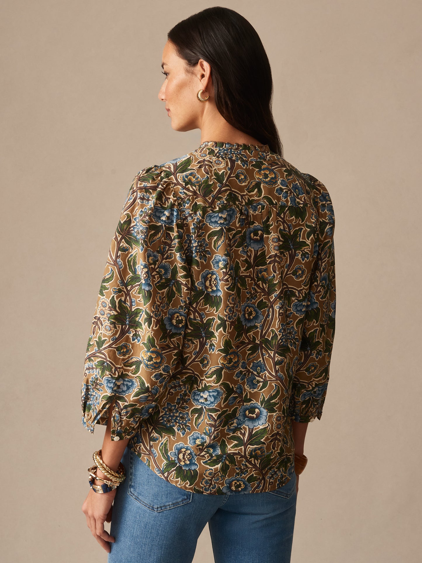 Woman wearing Josette Blouse in Bucolic Blooms by J.McLaughlin, featuring a floral pattern in earthy tones, paired with blue jeans, embodying effortlessly stylish, enduring designs.