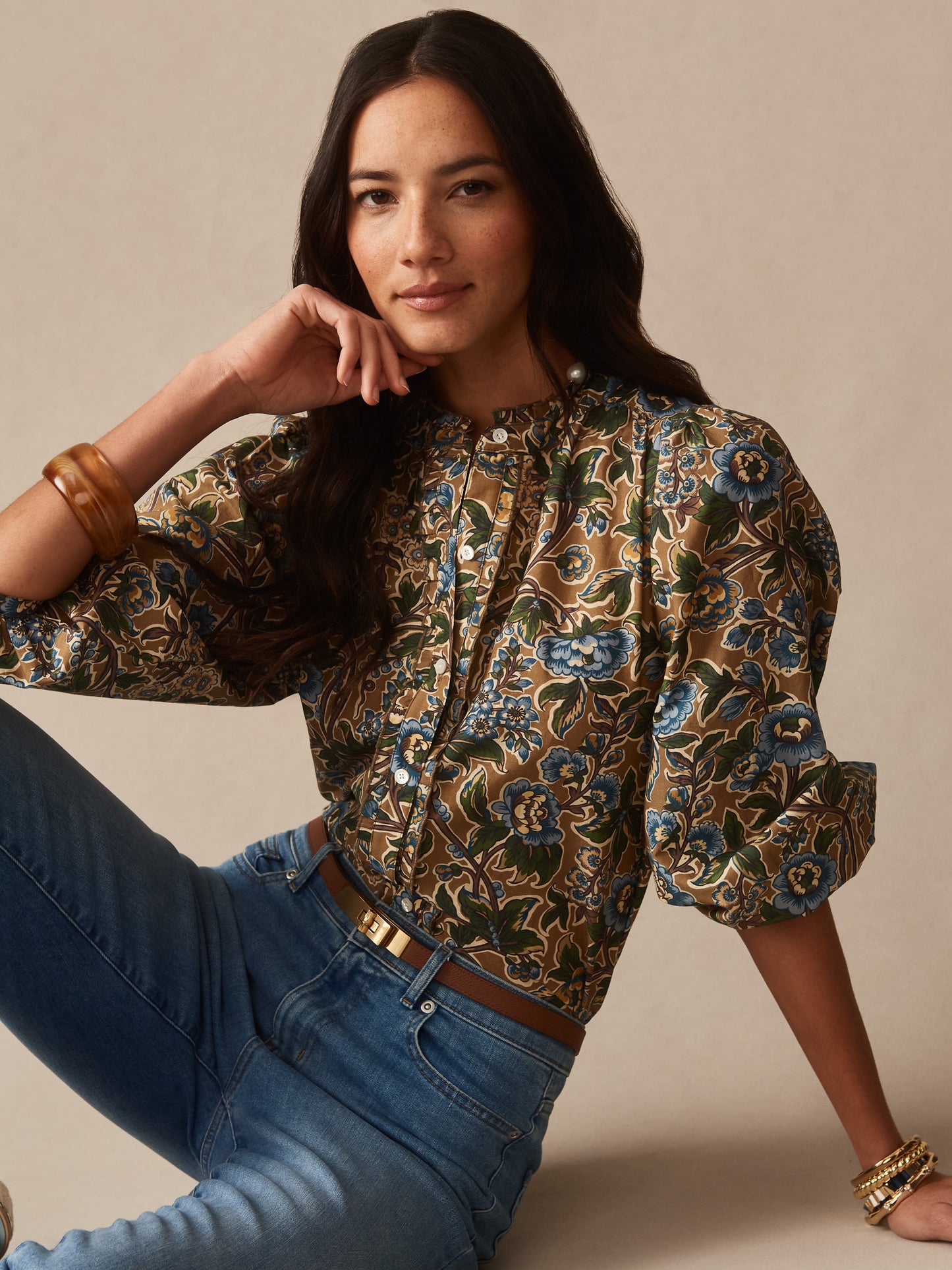 Woman wearing Josette Blouse in Bucolic Blooms by J.McLaughlin, featuring floral print with blue and green tones, styled with jeans and wooden bangles, embodying effortlessly stylish, enduring designs. A destination for defining style. Life, Well-Lived.
