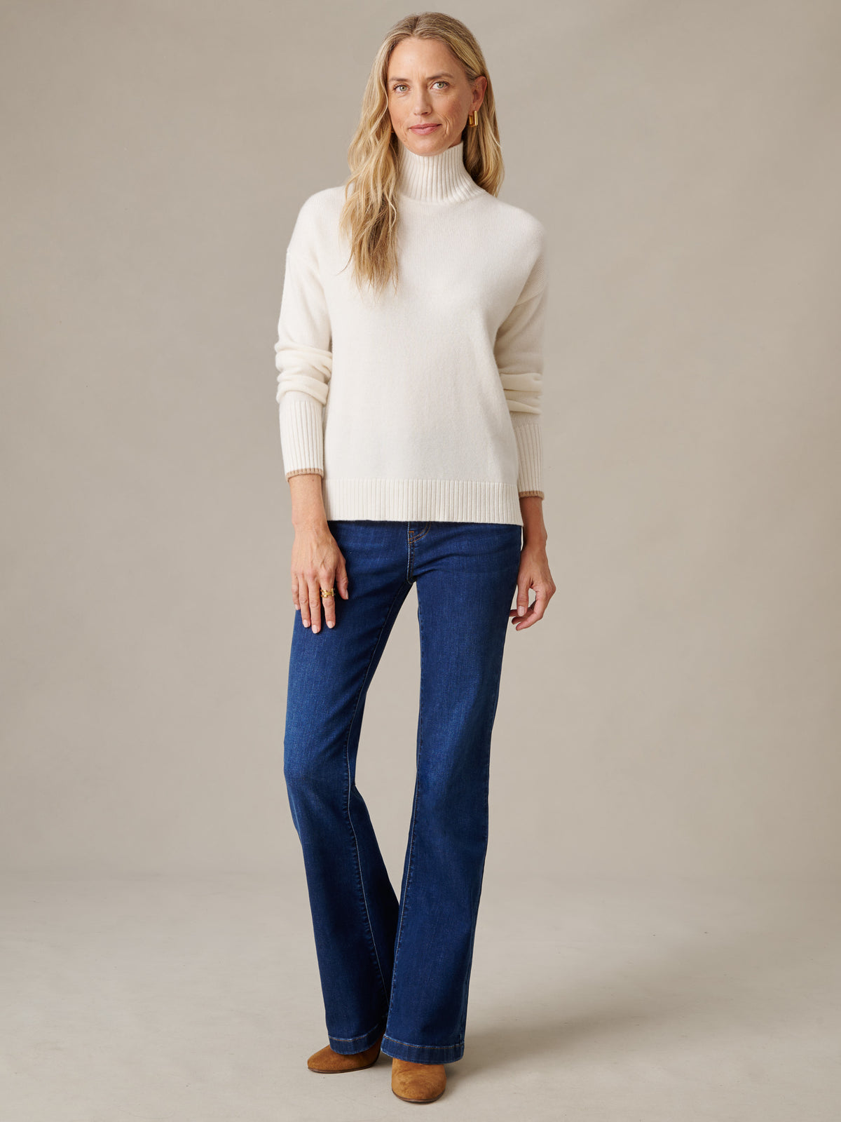 J.McLaughlin Dina Cashmere Turtleneck in ivory styled with dark blue jeans on a woman standing in a neutral studio setting