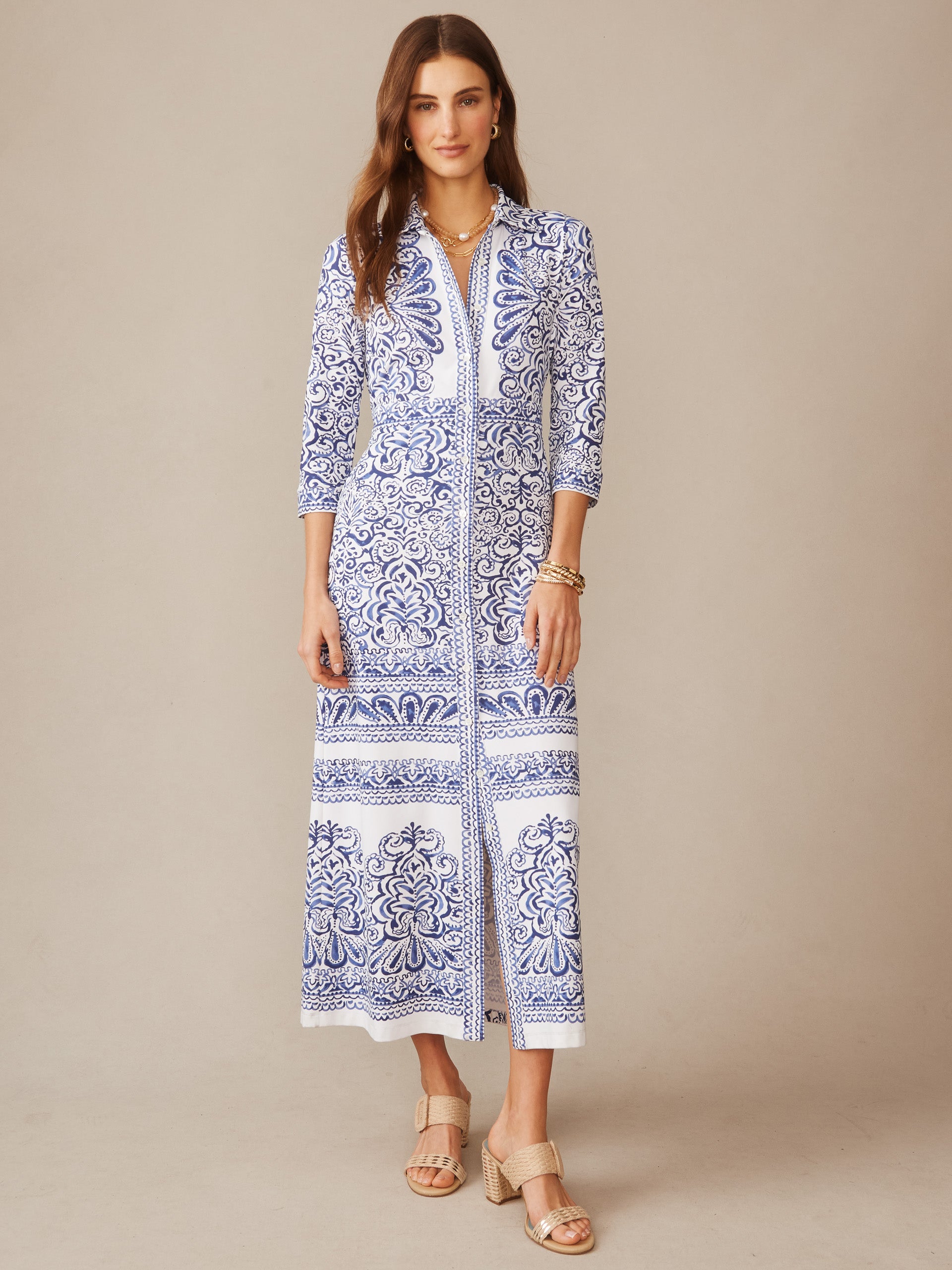 A model wears the Kailyn Maxi Dress in Faiz Frame by J.McLaughlin, featuring an intricate blue and white pattern, three-quarter sleeves, and a front slit, showcasing effortlessly stylish and enduring designs through innovative fabrics and a legacy of timeless fashion. A destination for defining style. Life, Well-Lived.