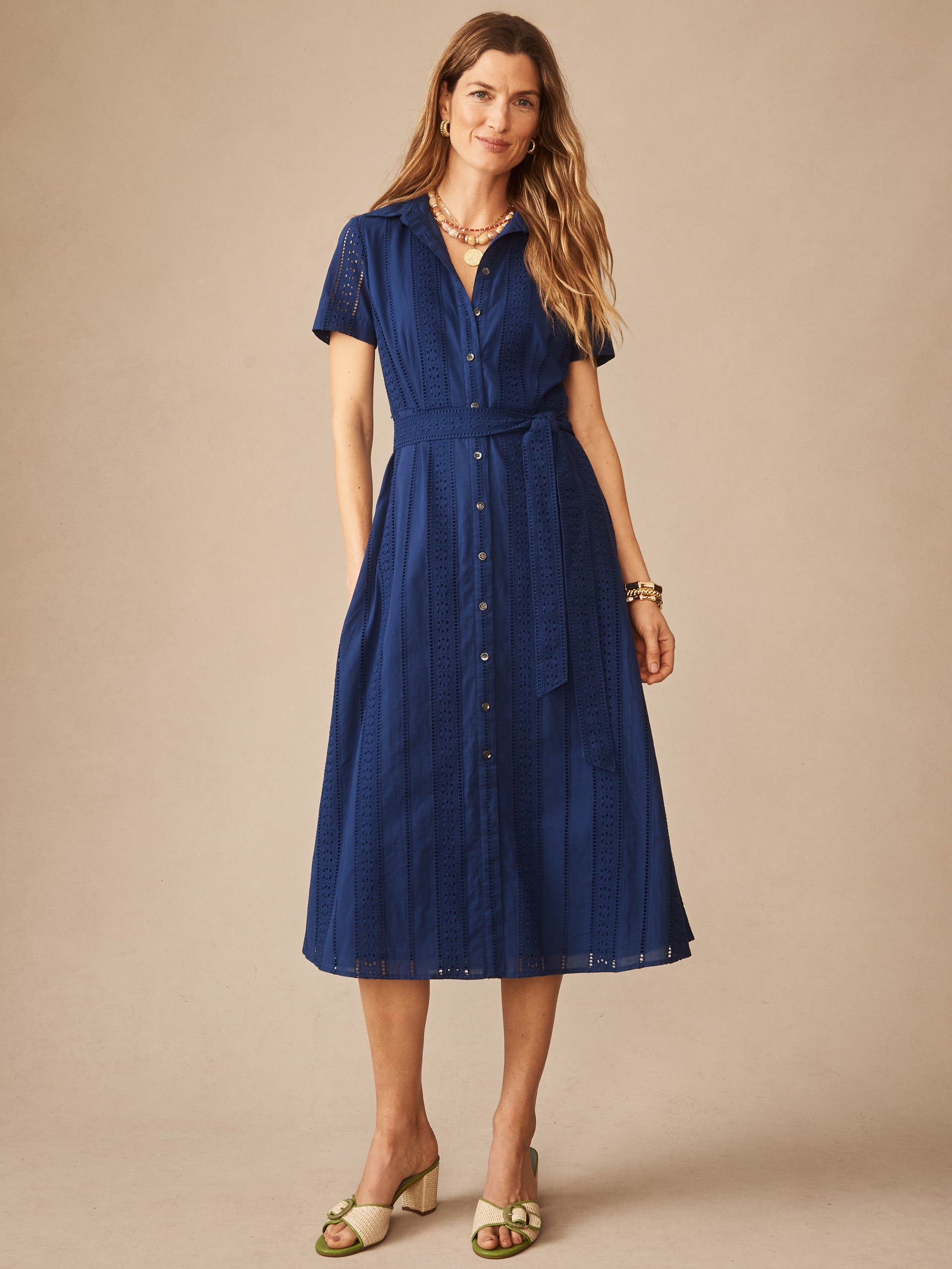 Woman wearing a navy blue Kalinda Dress in Eyelet by J.McLaughlin, featuring button-front, short sleeves, and a tie waist, embodying effortlessly stylish, enduring designs in innovative fabrics.