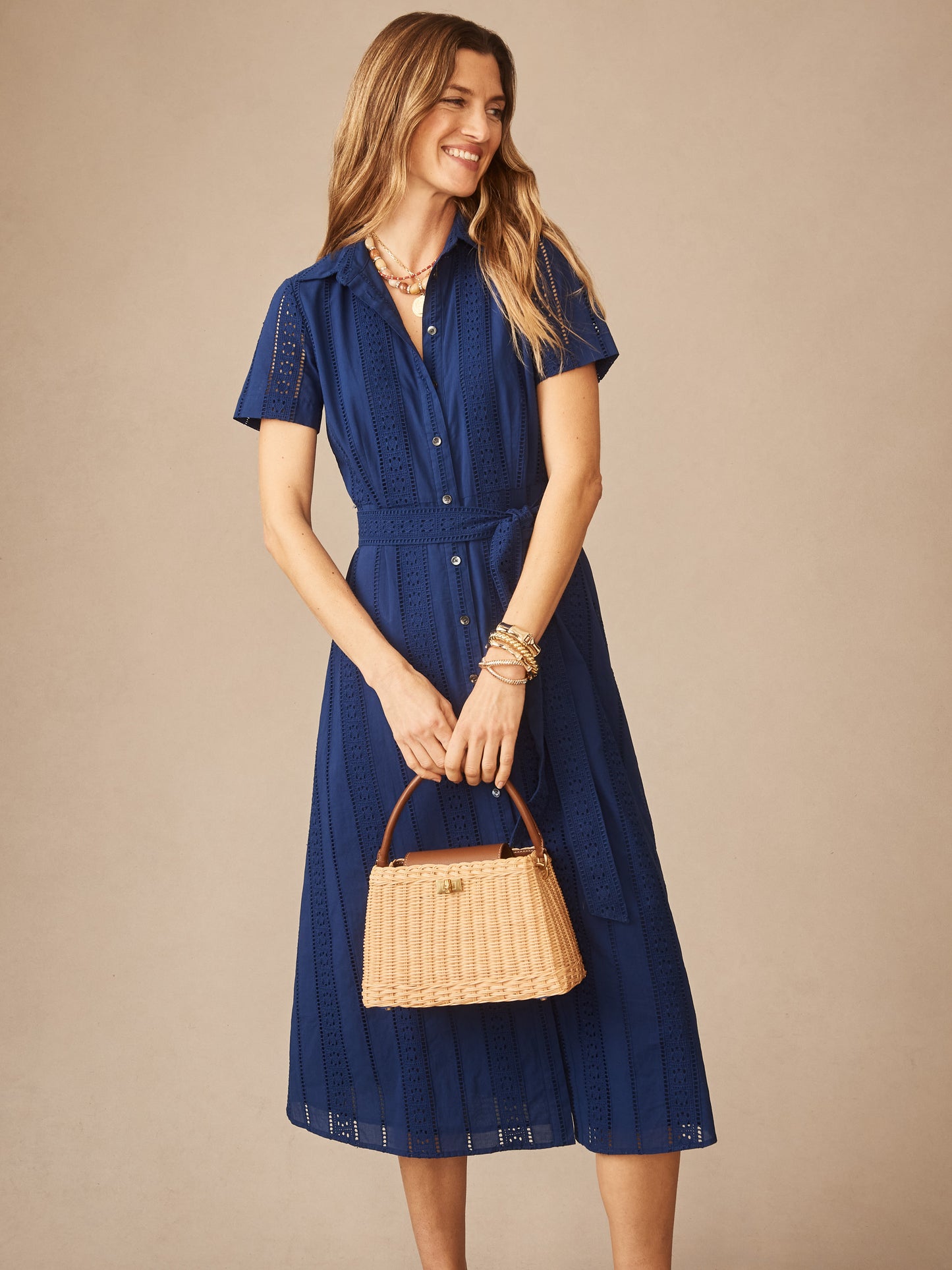 Woman wearing a navy Kalinda Dress in Eyelet by J.McLaughlin, styled with bracelets and a woven handbag, showcasing effortlessly stylish and enduring designs for a destination for defining style. Life, Well-Lived.