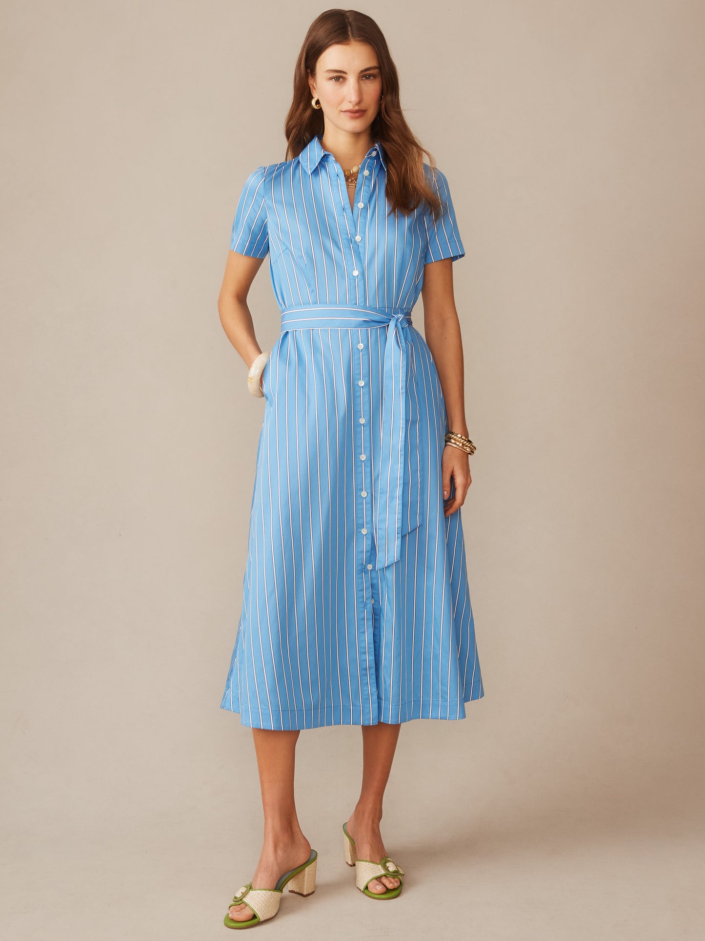 Woman wearing Kalinda Dress in Stripe by J.McLaughlin, a blue and white striped shirt dress with short sleeves and a waist tie, showcasing effortlessly stylish, enduring designs and innovative fabrics. A destination for defining style. Life, Well-Lived.