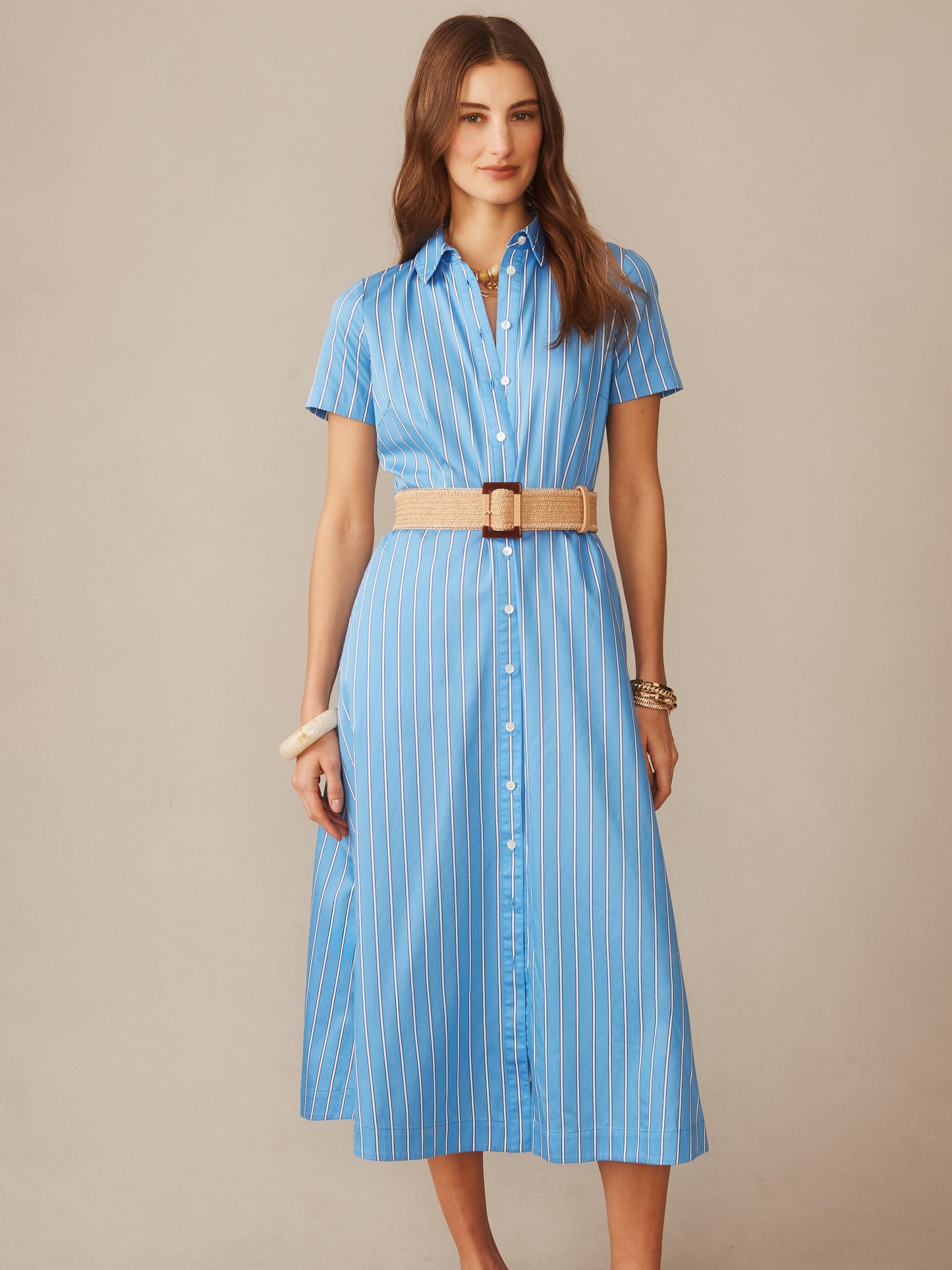 Woman wearing a blue and white striped Kalinda Dress in Stripe by J.McLaughlin, styled with a woven beige belt and bracelets, showcasing effortlessly stylish, enduring designs.