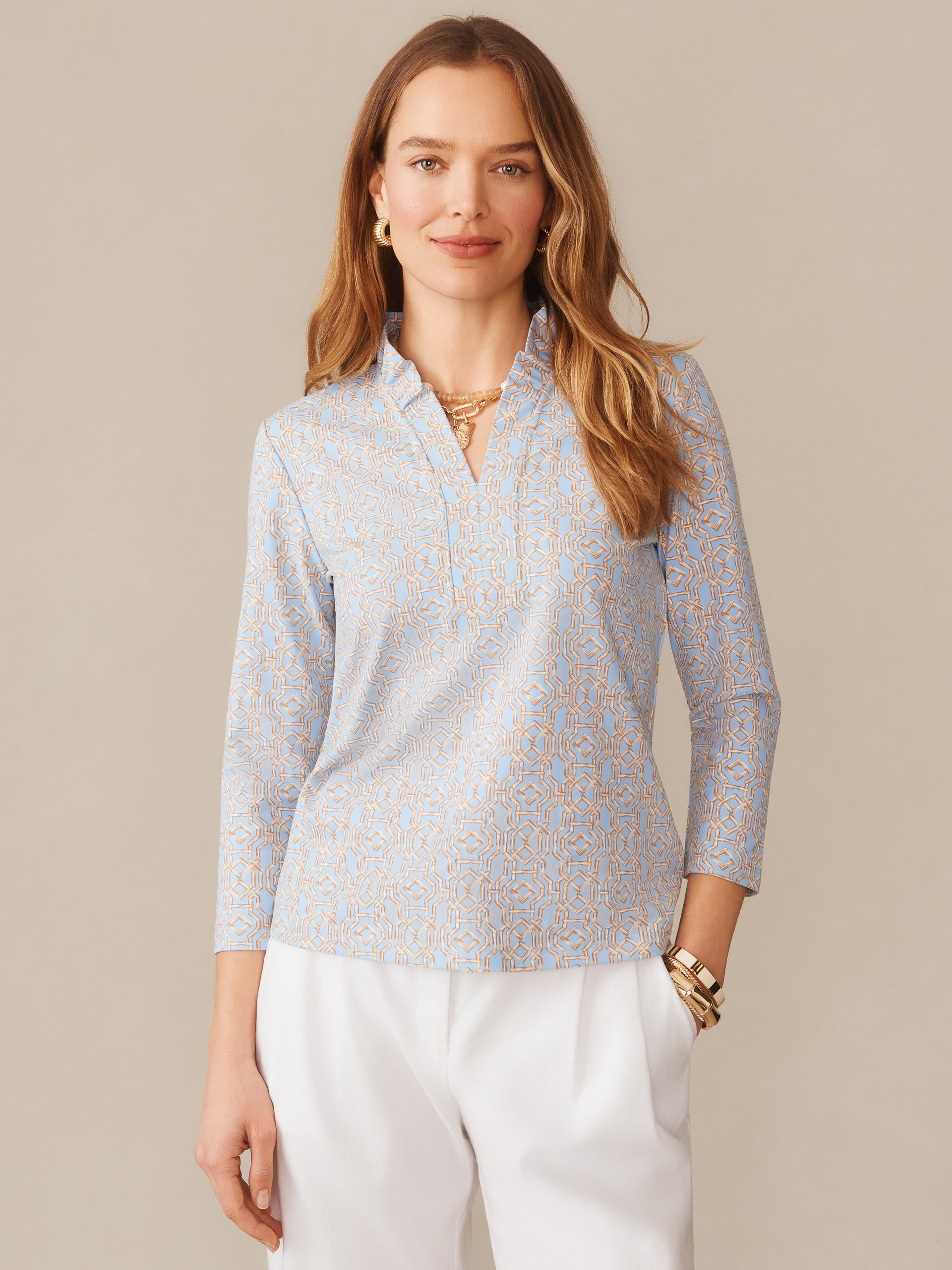 Woman wearing the Kate Ruffle Top in Bamboo Lane by J.McLaughlin, featuring a subtle blue and tan geometric pattern, paired with white pants, embodying effortlessly stylish, enduring designs with innovative fabrics and a legacy of timeless fashion. A destination for defining style. Life, Well-Lived.