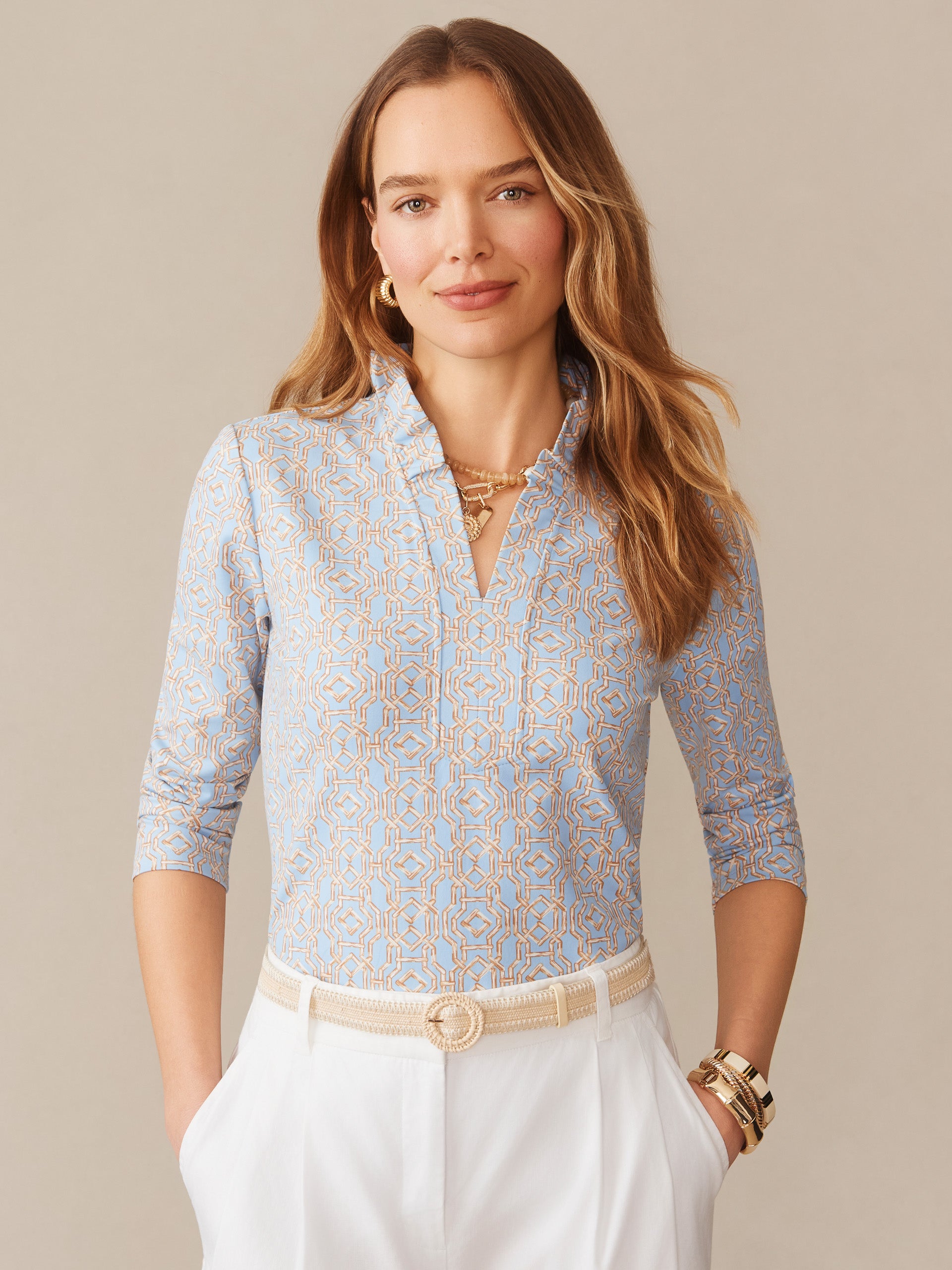 Woman wearing a blue and tan patterned Kate Ruffle Top in Bamboo Lane by J.McLaughlin, styled with white pants and gold jewelry, showcasing effortlessly stylish, enduring designs and innovative fabrics at a destination for defining style. Life, Well-Lived.