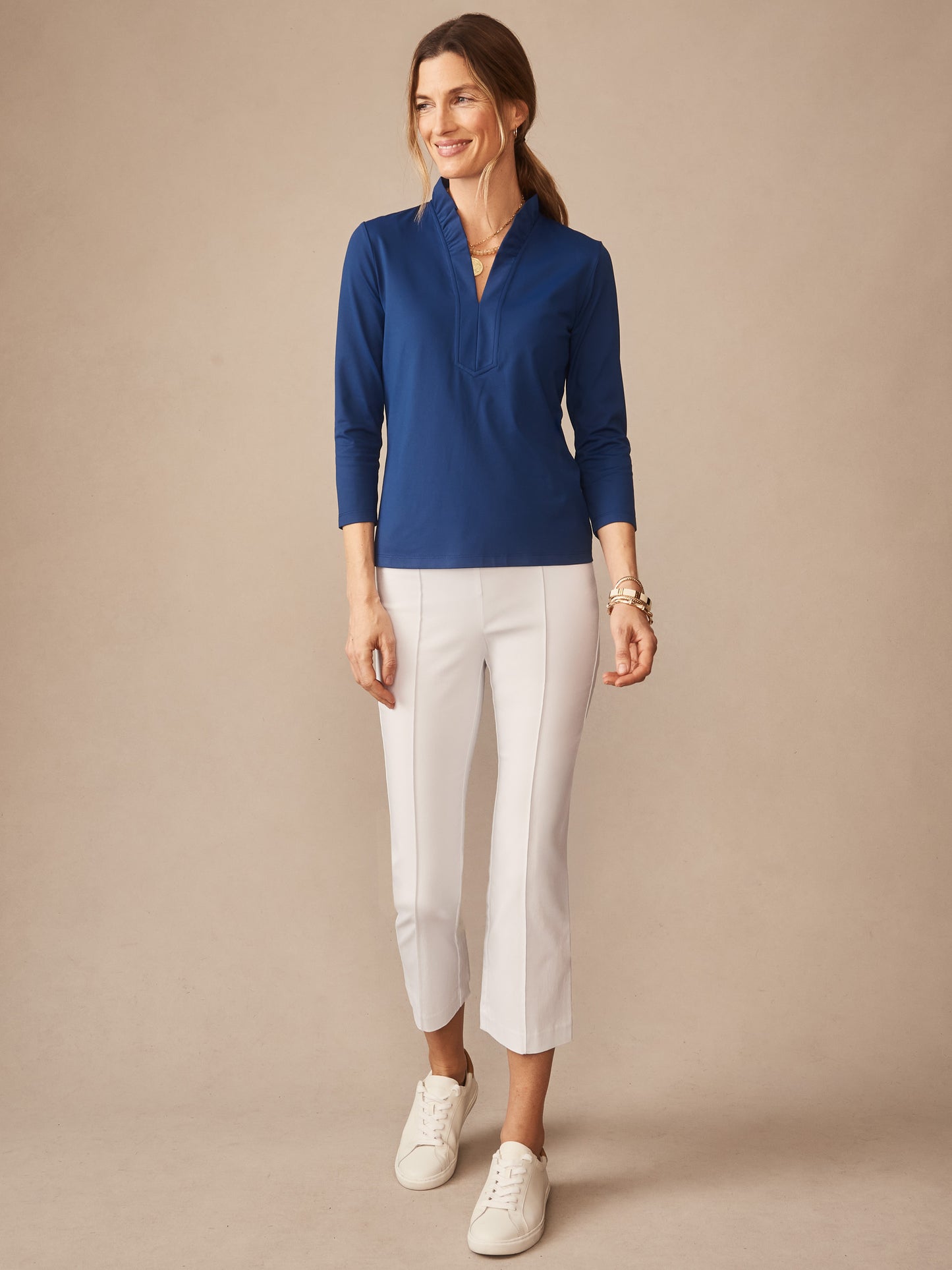 Woman wearing a nautical navy Kate Ruffle Top from J.McLaughlin paired with white cropped pants and sneakers, showcasing effortlessly stylish, enduring designs. A destination for defining style. Life, Well-Lived.