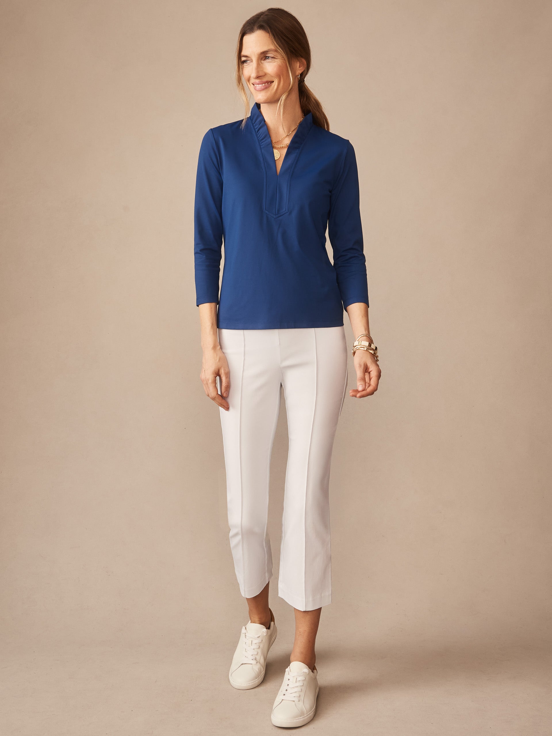 Woman wearing a nautical navy Kate Ruffle Top from J.McLaughlin paired with white cropped pants and sneakers, showcasing effortlessly stylish, enduring designs. A destination for defining style. Life, Well-Lived.