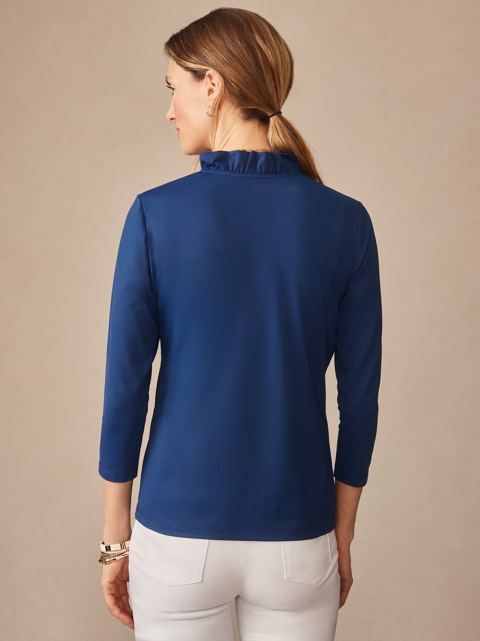 Woman seen from behind wearing a nautical navy Kate Ruffle Top by J.McLaughlin with three-quarter sleeves and a delicate ruffle collar, showcasing effortlessly stylish and enduring designs.