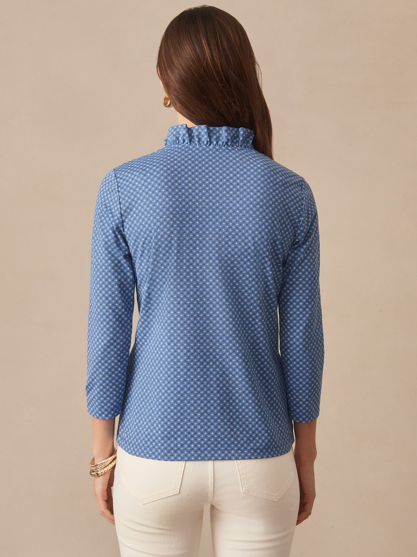 A woman wearing the Kate Ruffle Top in Bonneval by J.McLaughlin in a blue patterned fabric, showcasing the back with a ruffled collar, reflecting effortlessly stylish, enduring designs and a legacy of timeless fashion. A destination for defining style. Life, Well-Lived.