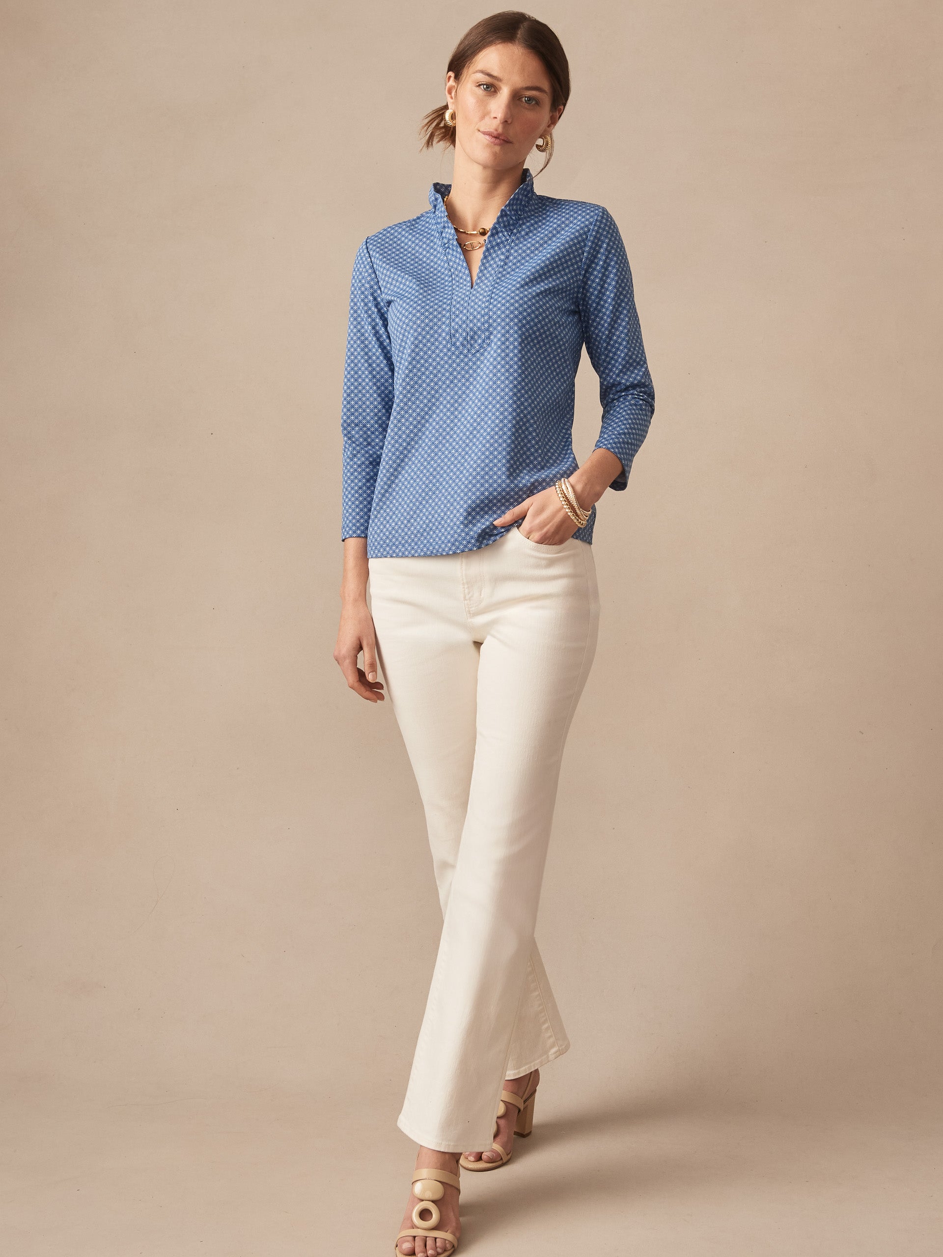 Woman wearing a J.McLaughlin Kate Ruffle Top in Bonneval with subtle ruffle details and a blue patterned fabric, styled with white pants and sandals, effortlessly stylish and enduring designs.