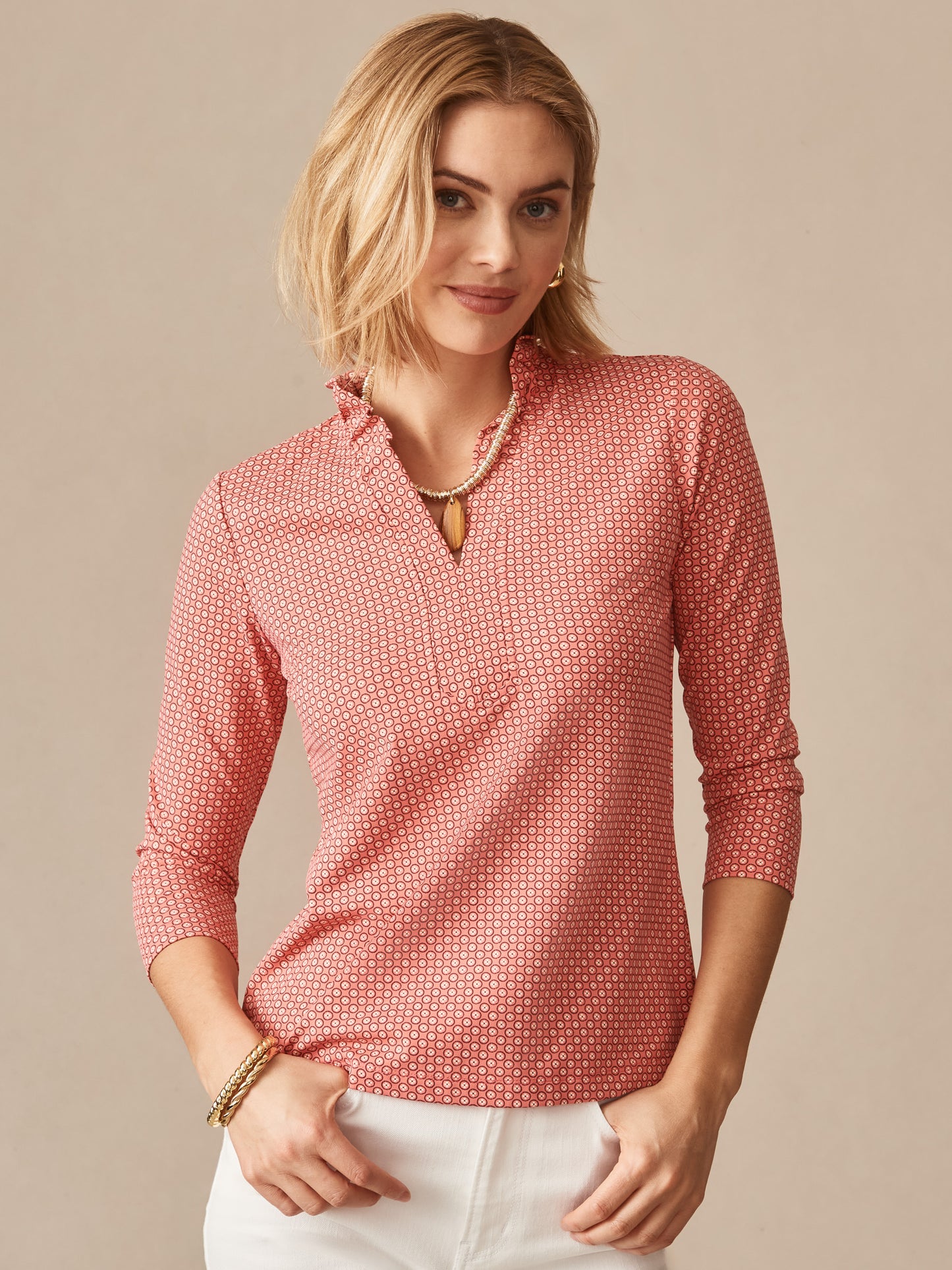 A woman wearing the Kate Ruffle Top in Bonneval by J.McLaughlin, featuring a subtle pattern in warm rose and off-white tones, embodies effortlessly stylish, enduring designs in a timeless blouse. A destination for defining style. Life, Well-Lived.