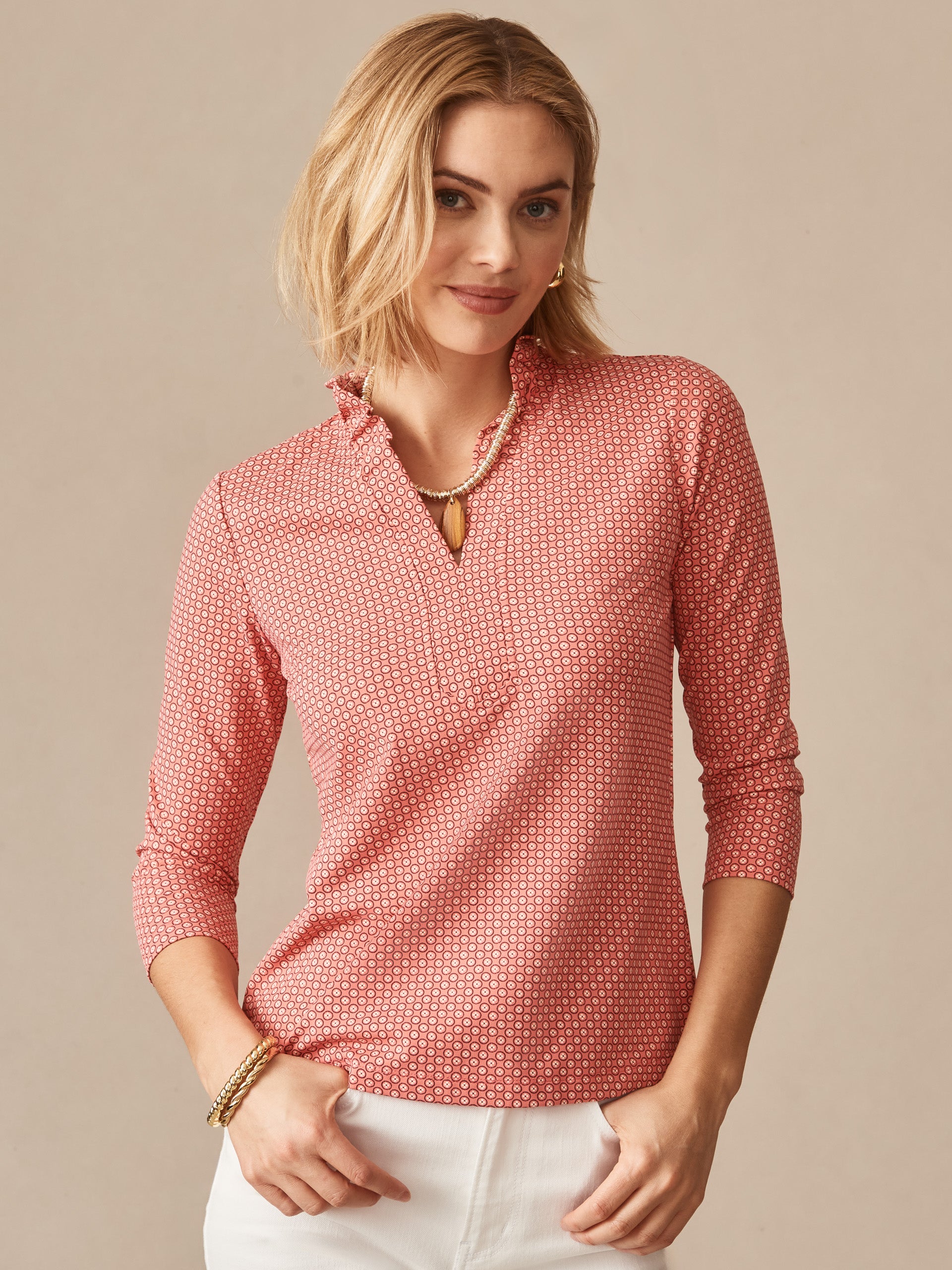 A woman wearing the Kate Ruffle Top in Bonneval by J.McLaughlin, featuring a subtle pattern in warm rose and off-white tones, embodies effortlessly stylish, enduring designs in a timeless blouse. A destination for defining style. Life, Well-Lived.