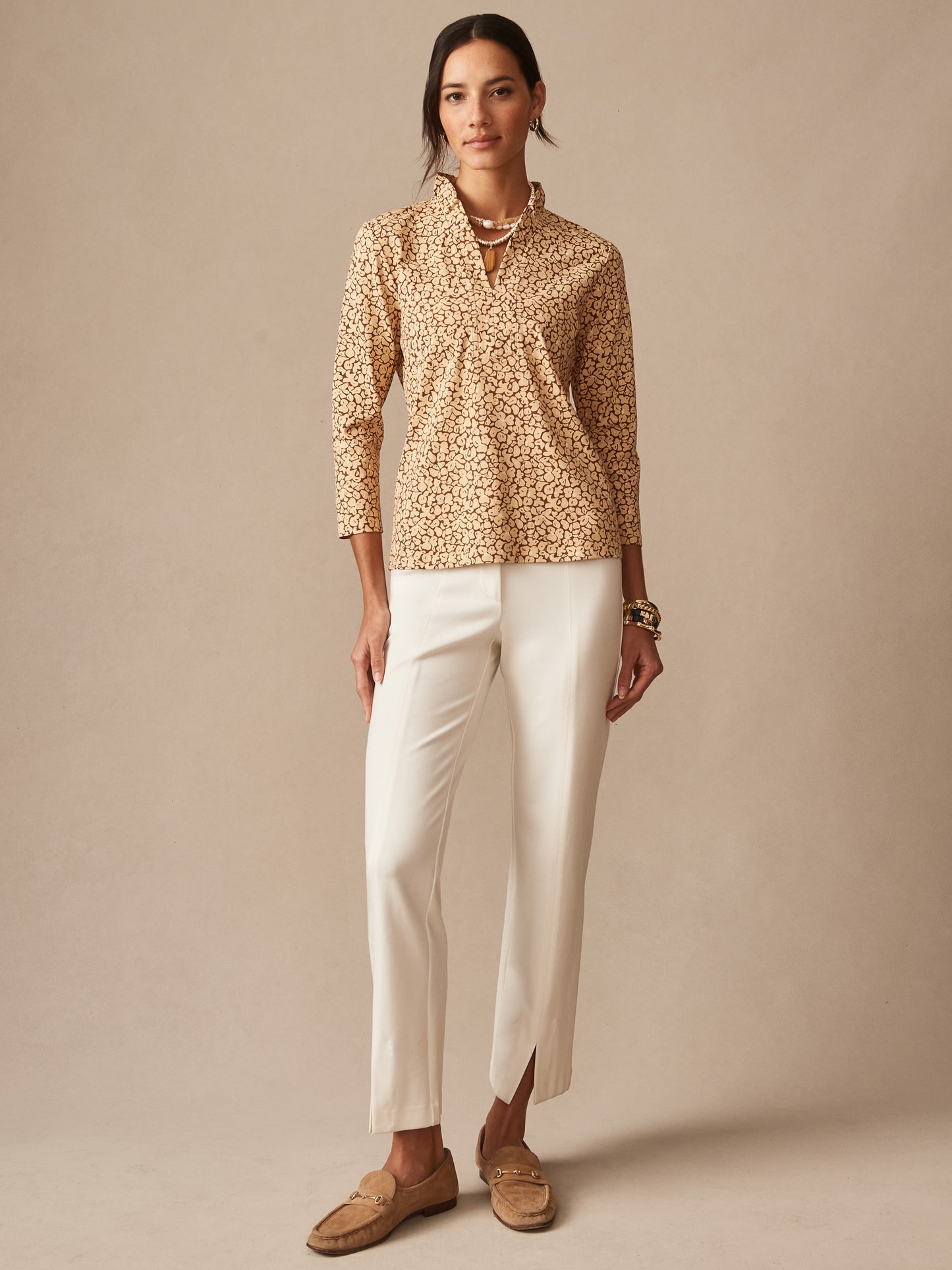 A woman wearing the Kate Ruffle Top in Celandine by J.McLaughlin, paired with white pants and loafers, showcasing effortlessly stylish, enduring designs and a legacy of timeless fashion. A destination for defining style. Life, Well-Lived.