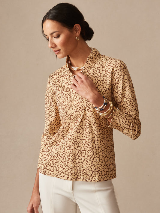 Woman wearing the Kate Ruffle Top in Celandine by J.McLaughlin, featuring a subtle floral pattern in warm tones, paired with white pants and gold accessories, epitomizing effortlessly stylish and enduring designs from a destination for defining style, life well-lived.