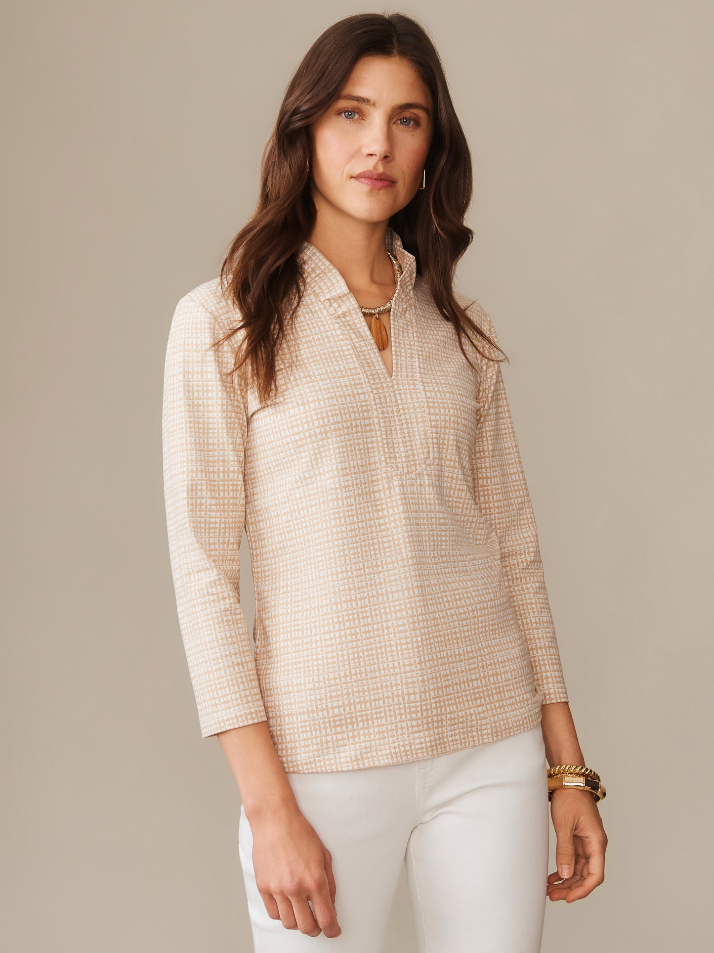 Woman wearing a lightweight, patterned Kate Ruffle Top in Pocket Square by J.McLaughlin, styled with white pants and gold accessories, showcasing effortlessly stylish, enduring designs.