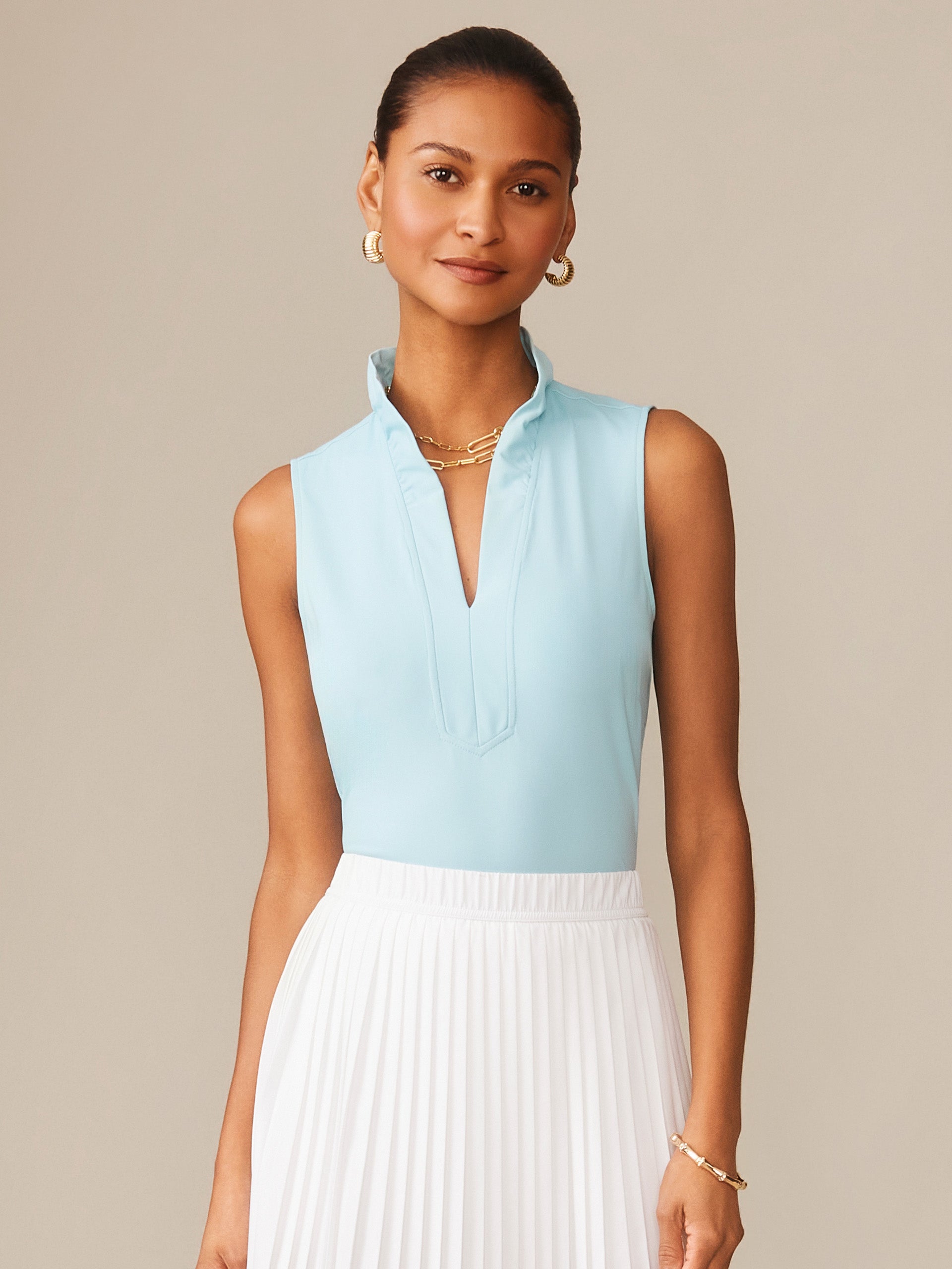 Woman wearing a light blue Kate Sleeveless Ruffle Top by J.McLaughlin paired with a white pleated skirt, showcasing effortlessly stylish, enduring designs and innovative fabrics.