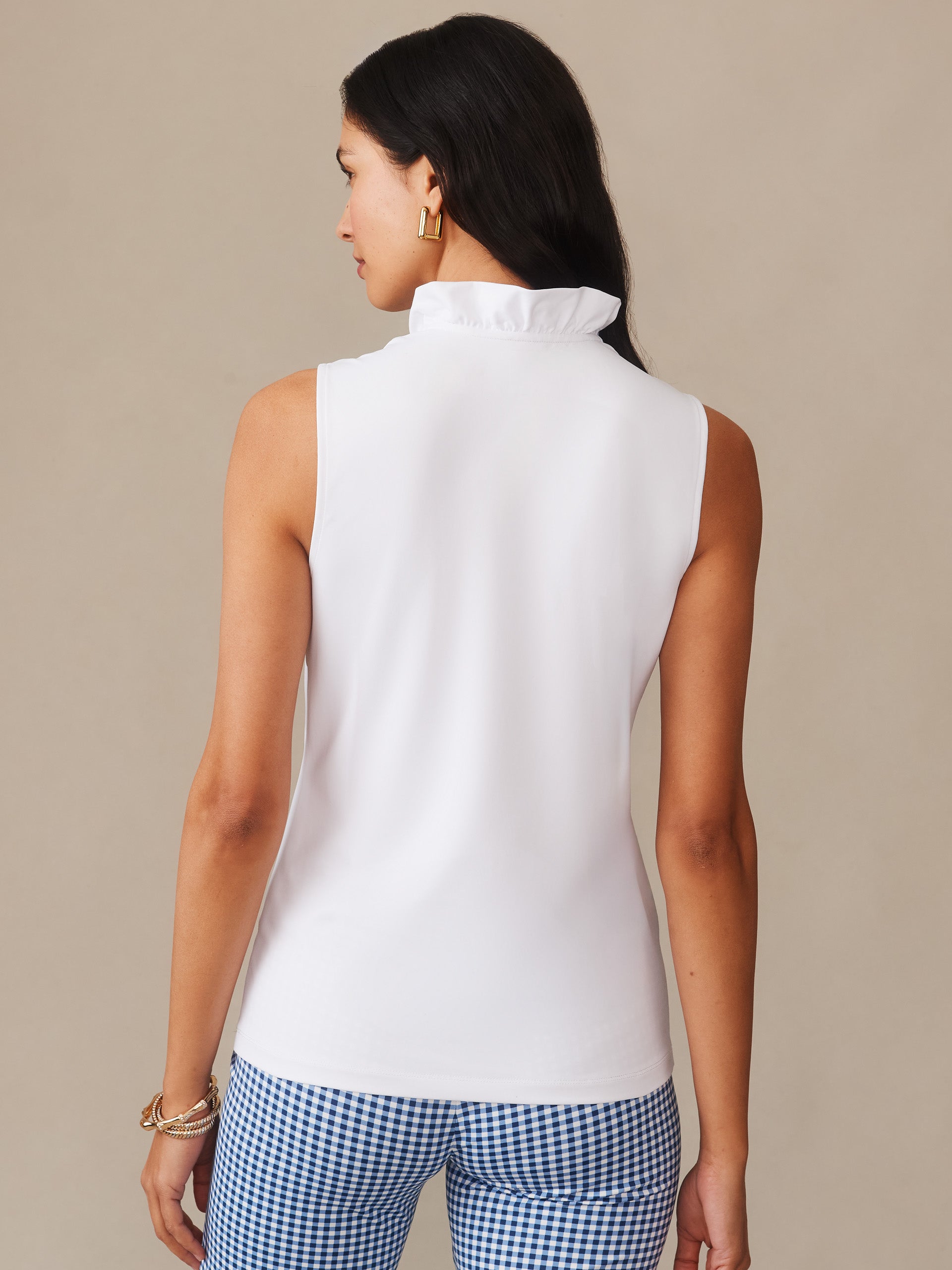 Woman wearing a white Kate Sleeveless Ruffle Top by J.McLaughlin, paired with blue gingham pants, showcasing effortlessly stylish, enduring designs with innovative fabrics.